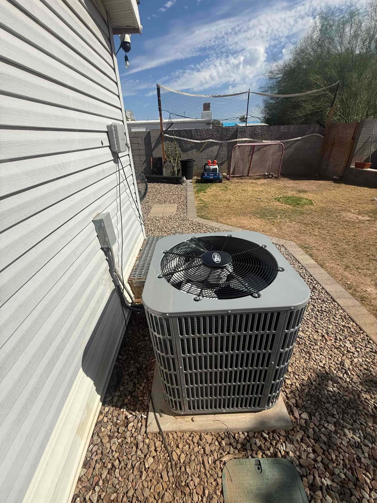 New outdoor condenser set on a level pad with insulated line set and electrical disconnect mounted on the exterior wall.