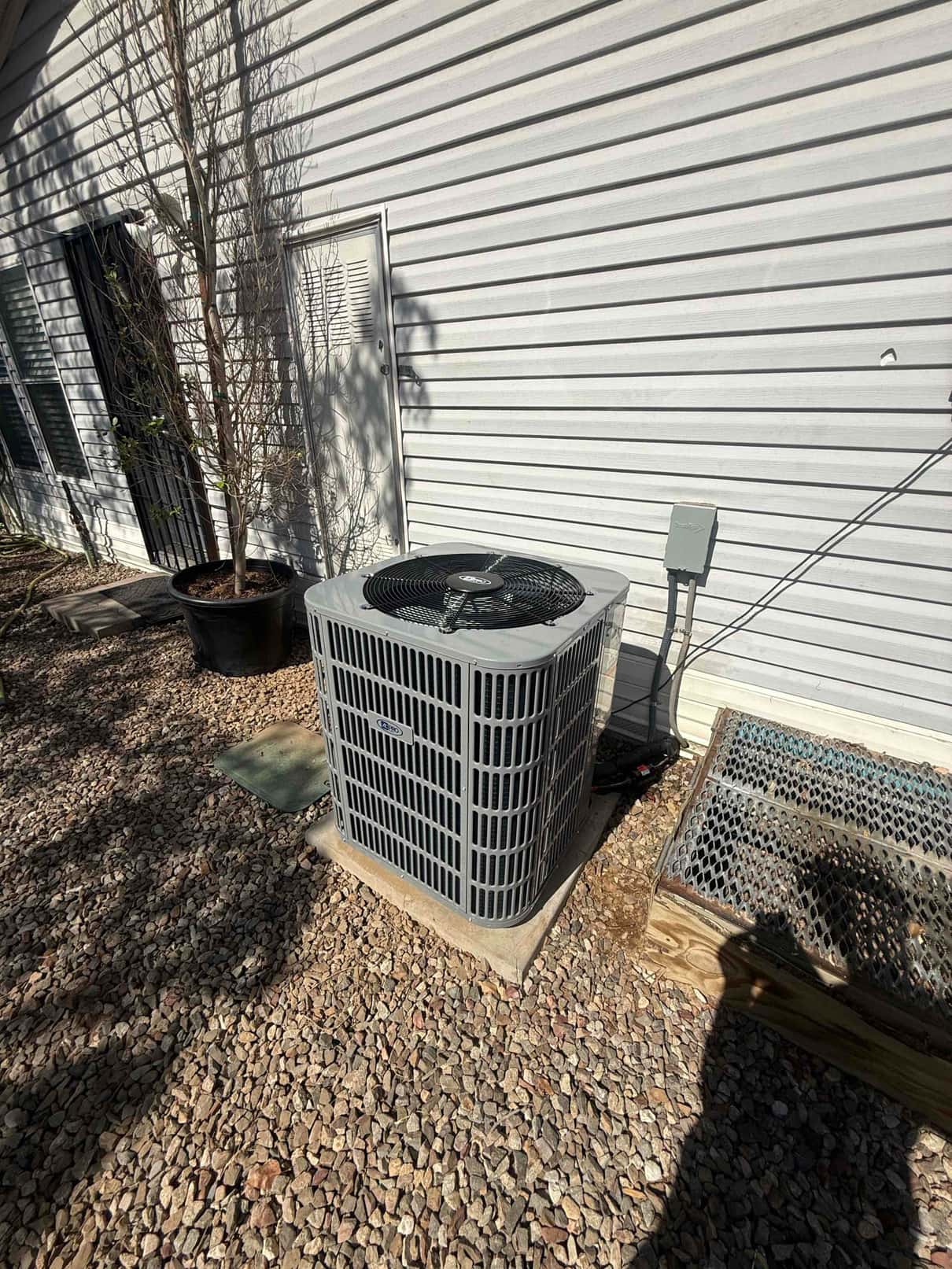 New outdoor condenser set on a level pad with insulated line set and exterior disconnect mounted on the wall.