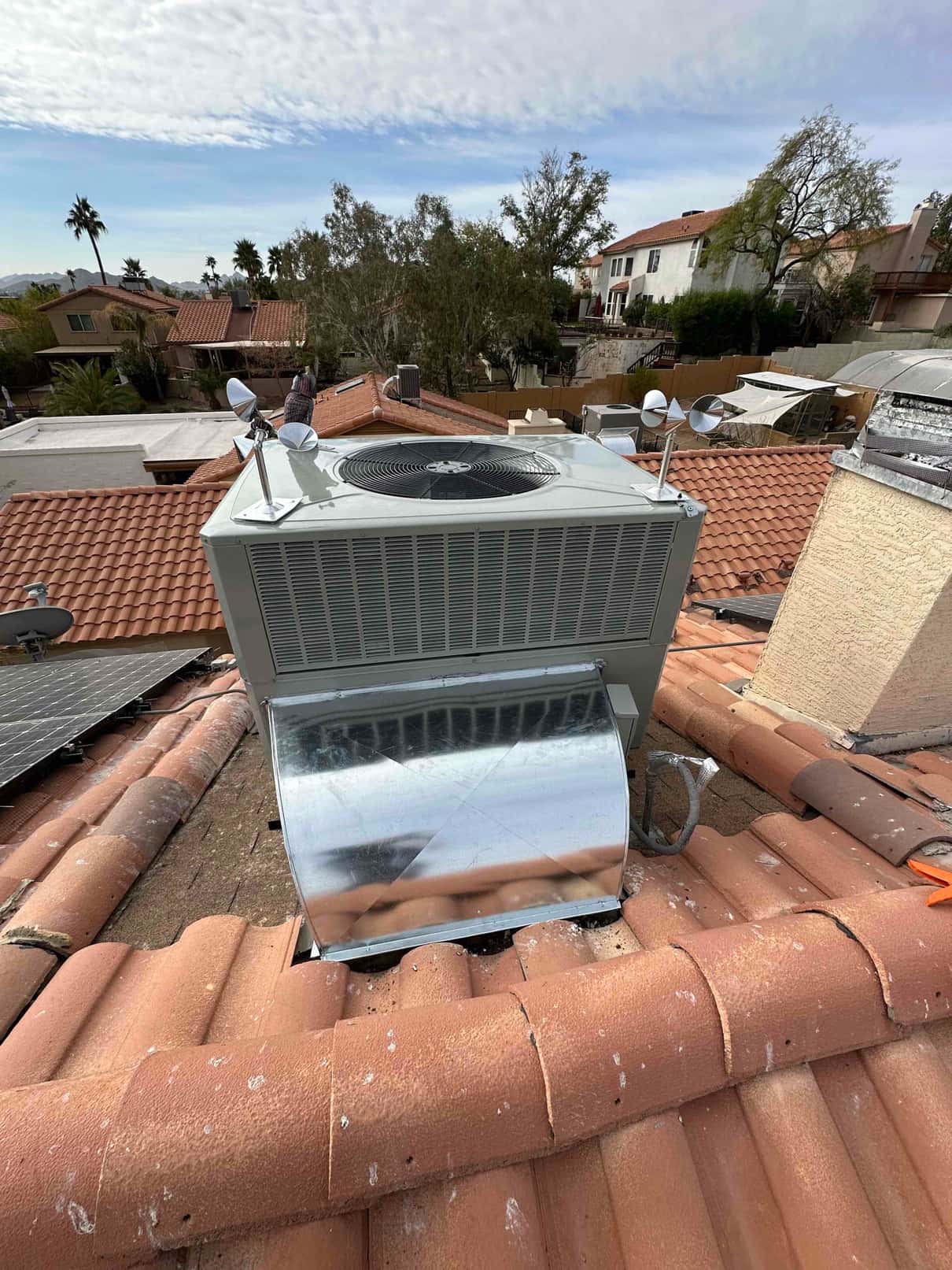 New rooftop heat pump set on tile roof with duct transition and secured electrical whip routed to the unit.