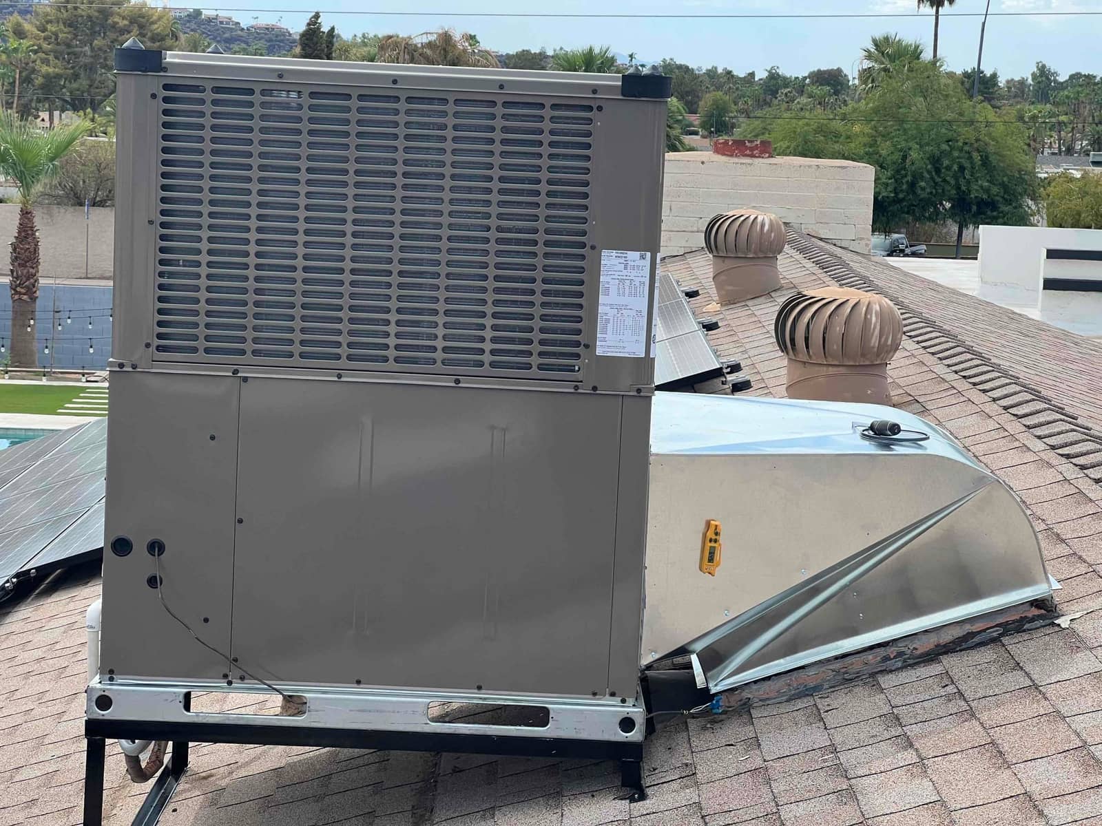 New rooftop package heat pump set on a stand with sealed curb adapter and insulated refrigerant penetrations on shingle roof.