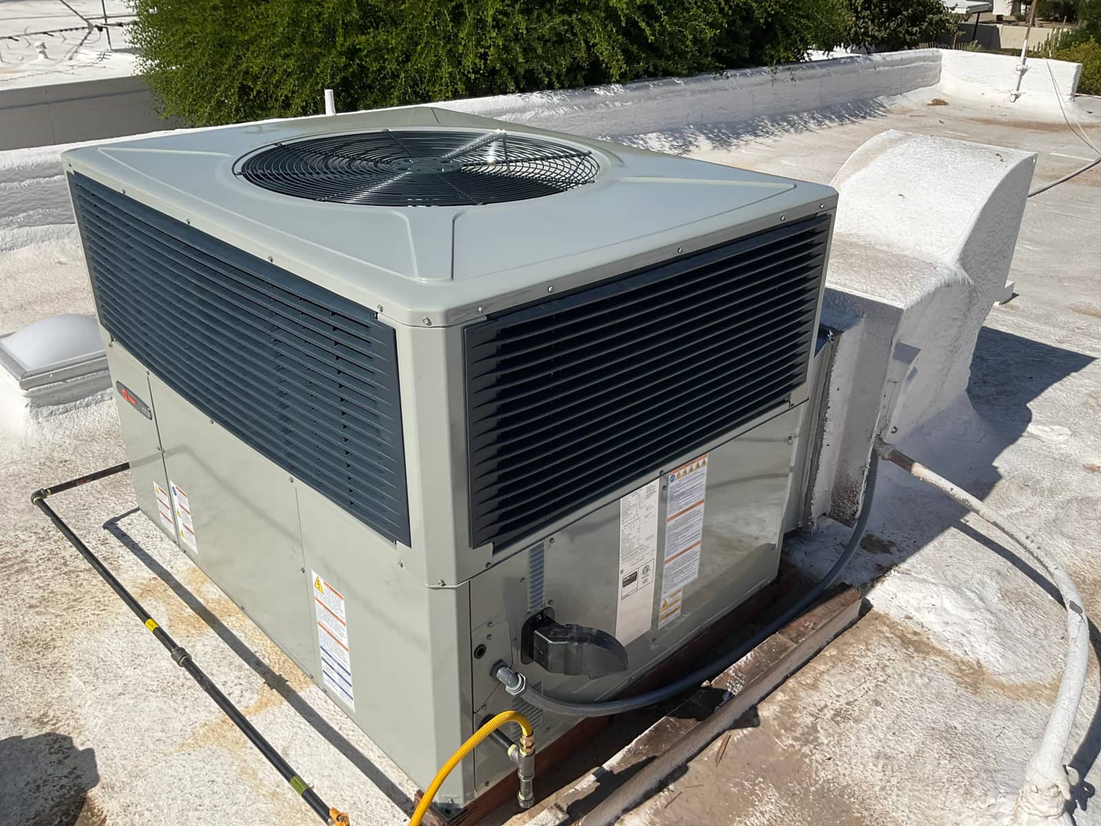 New rooftop package HVAC unit set on curb with connected gas line, condensate drain, and flexible electrical conduit.