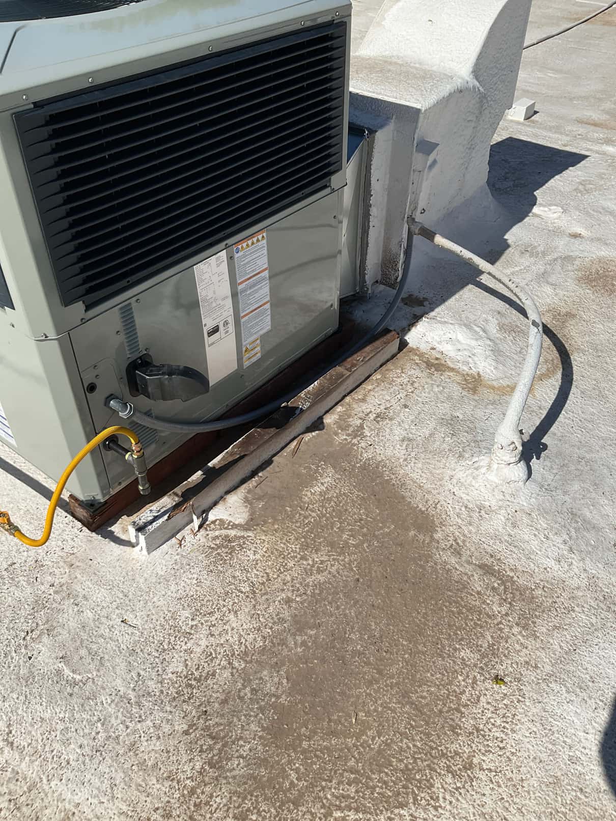 New rooftop package unit set on curb with gas connection, electrical whip, and sealed roof penetration visible.
