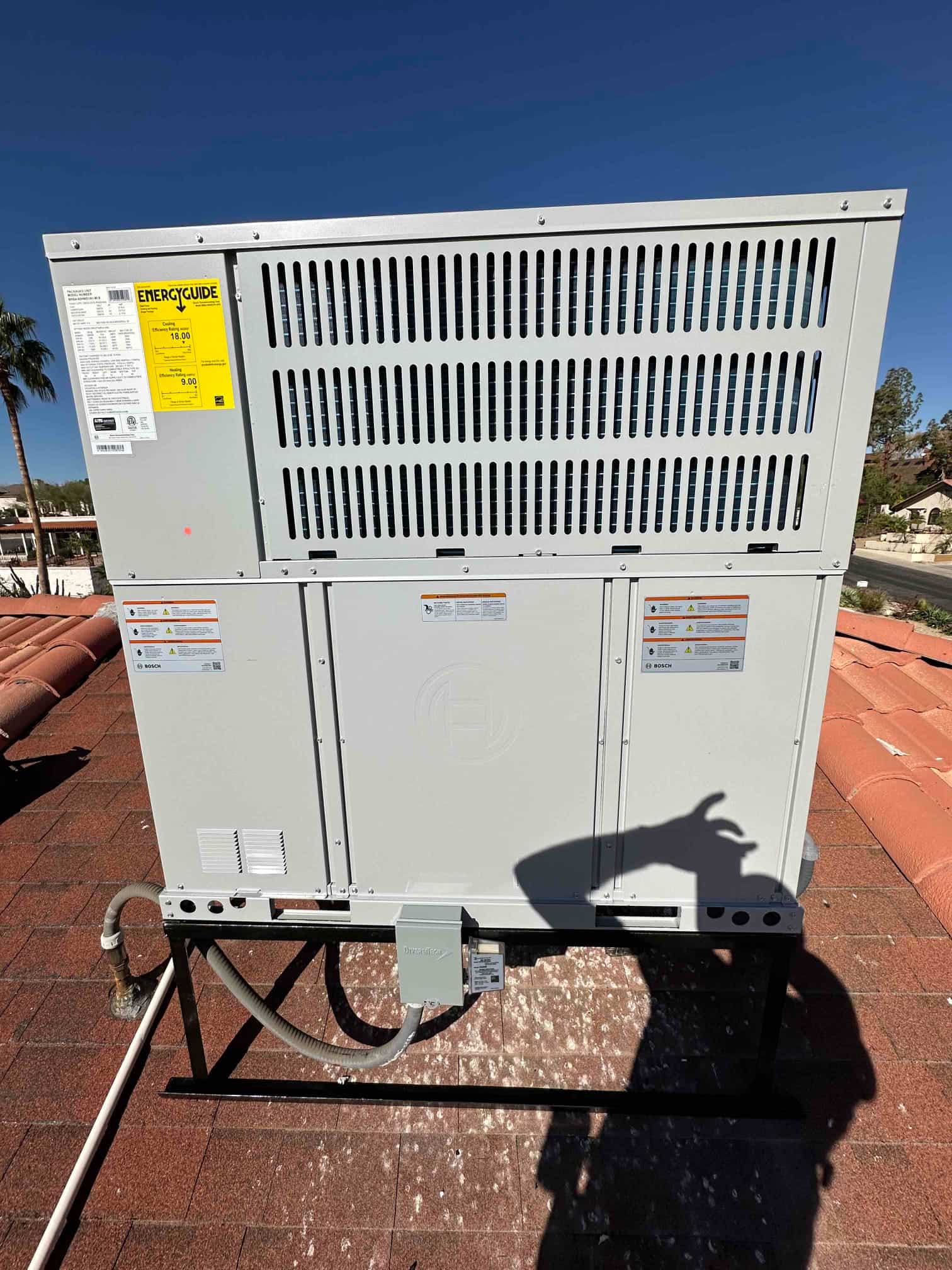 New rooftop packaged heat pump set on a metal stand with connected electrical disconnect and drain line routing.
