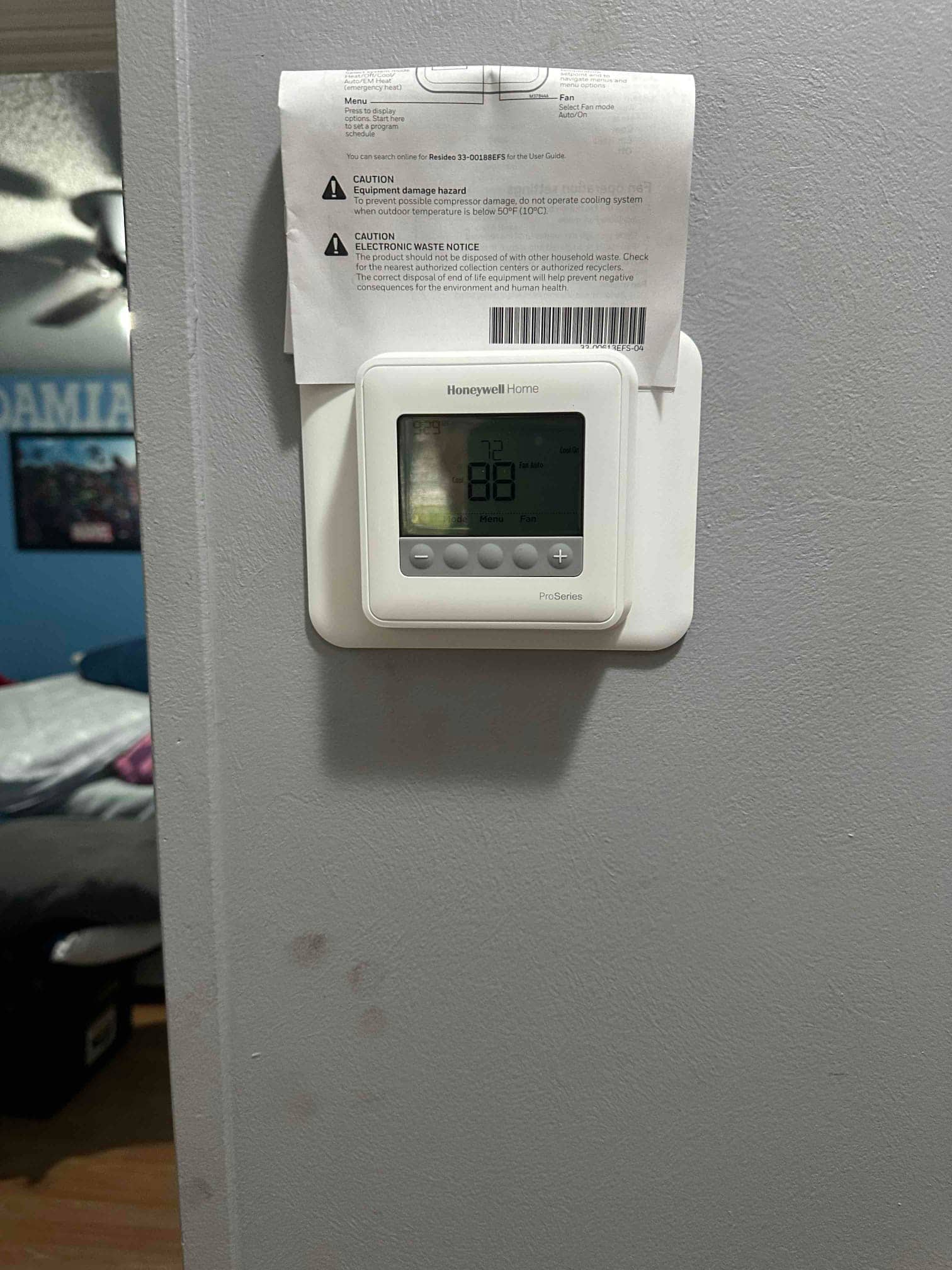 New wall-mounted thermostat installed with user guide attached, displaying room temperature and system mode indicators.
