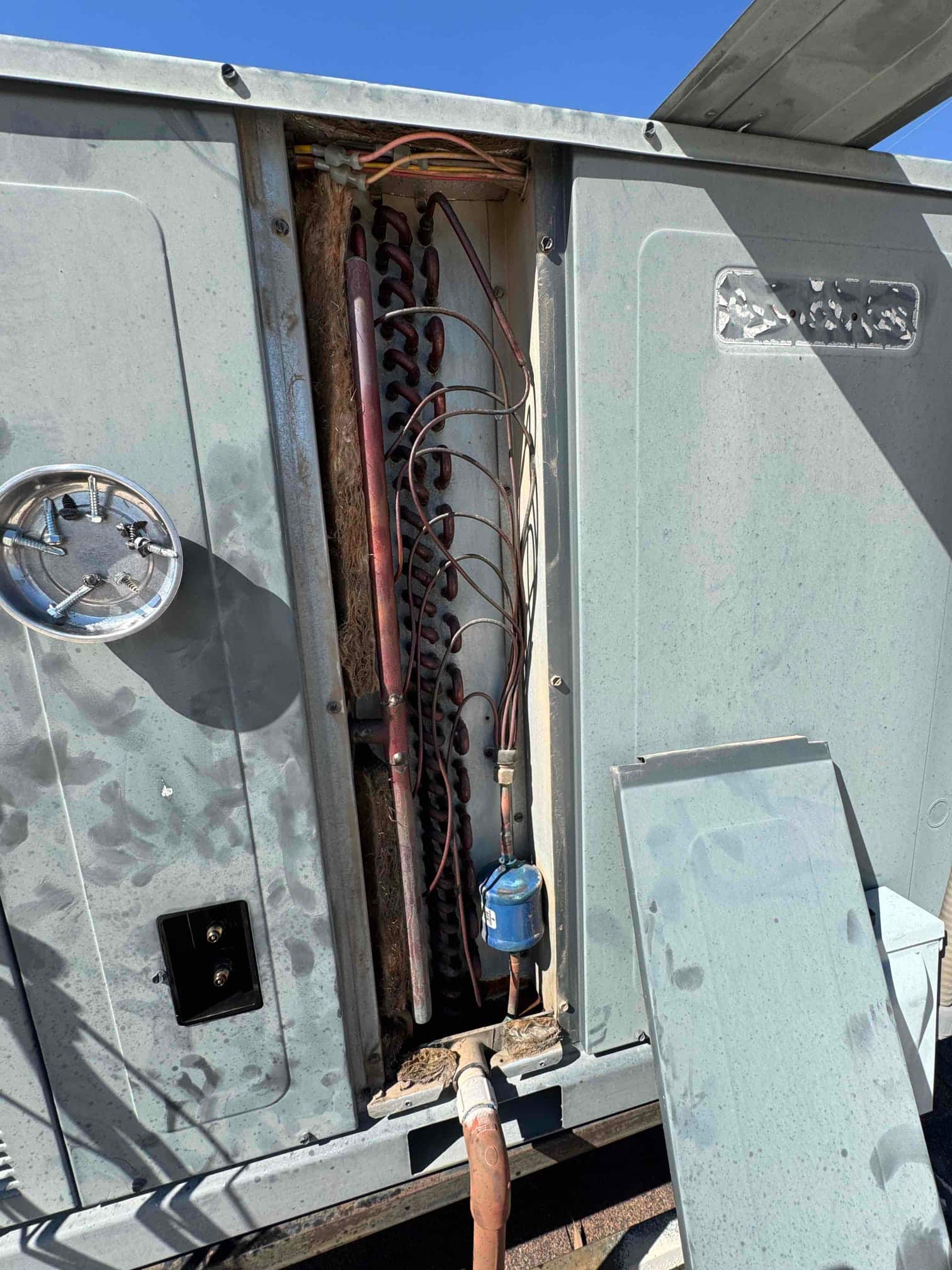 Open condenser access panel exposes contactor, wiring, and copper refrigerant lines, with the cover removed and resting against the unit.