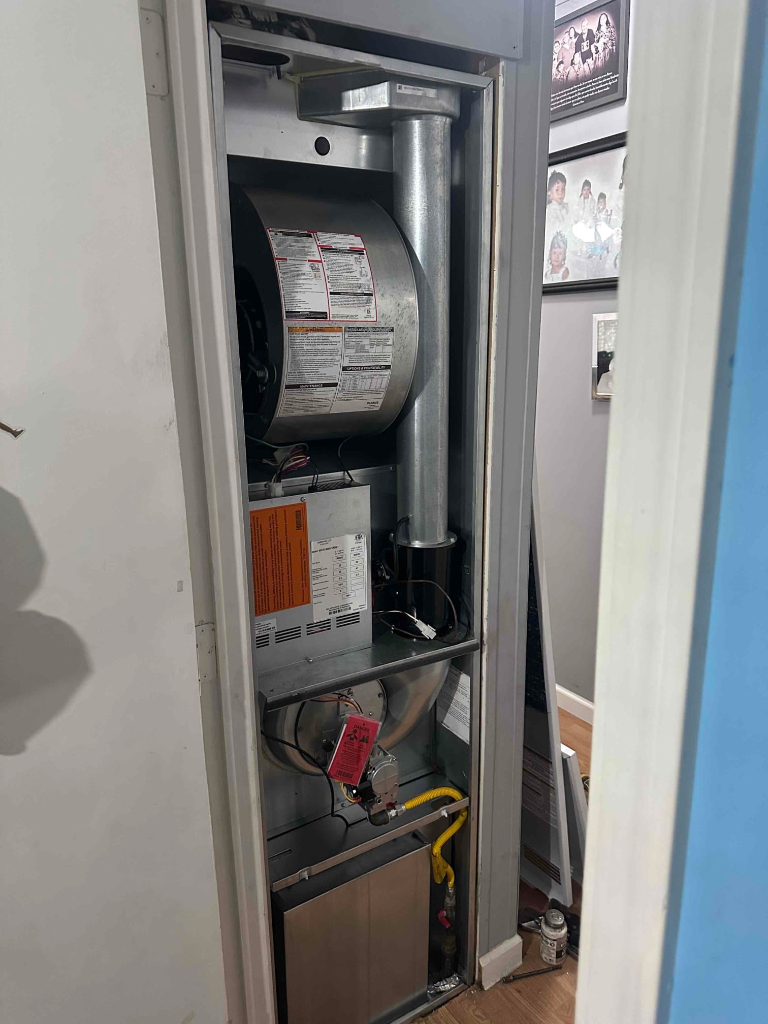 Open furnace cabinet shows blower assembly, gas valve with yellow flex connector, venting, and wiring during installation.