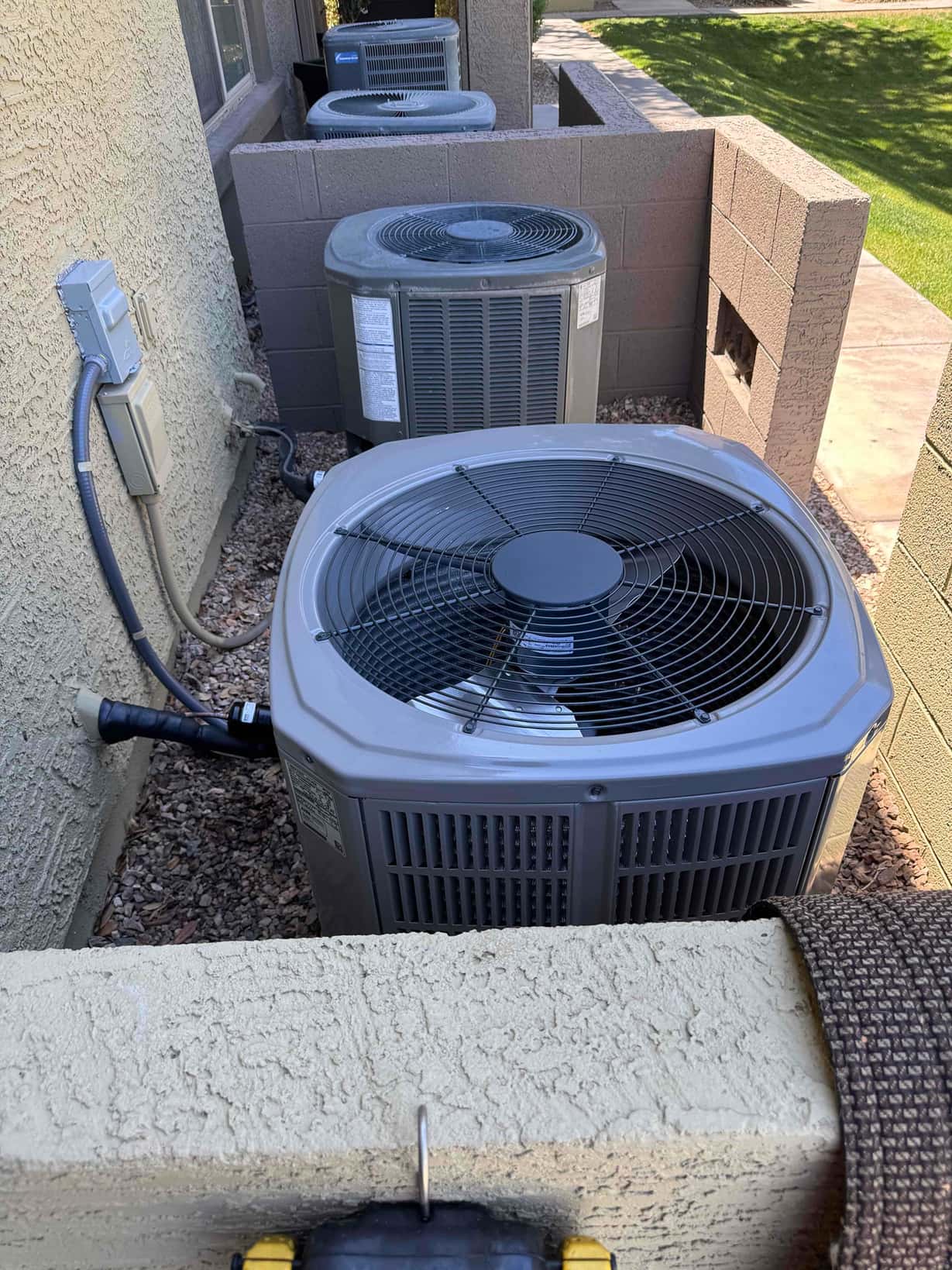 Two outdoor condensers set on level ground with electrical disconnects and insulated refrigerant lines along the exterior wall.