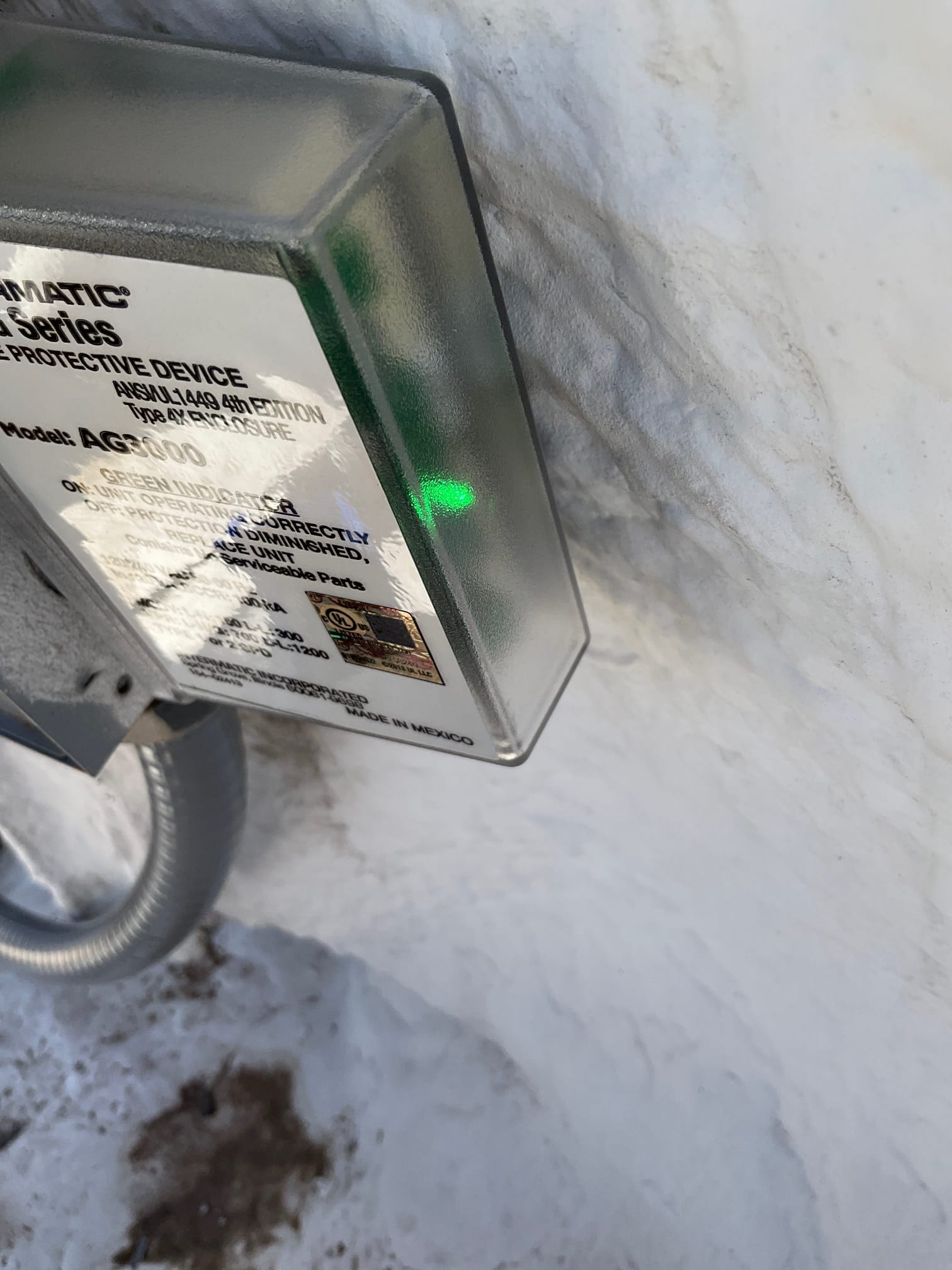 Outdoor surge protective device with green status indicator illuminated, mounted next to the HVAC equipment electrical conduit.