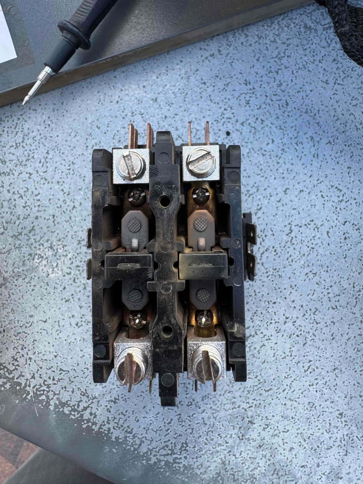 Removed 2-pole contactor showing worn contacts and screw terminals on a metal work surface during air conditioner repair.