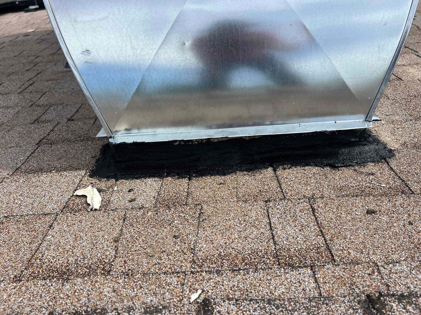 Roof curb or duct curb sealed to asphalt shingles with roofing mastic around the base for weatherproofing.