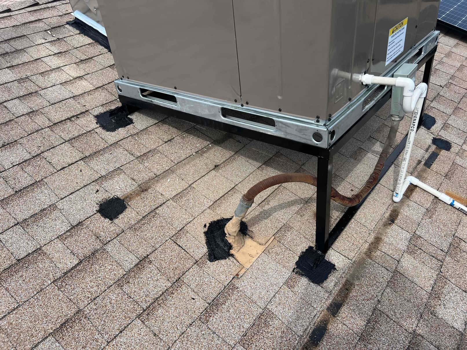 Roof-mounted package heat pump set on a metal stand with sealed penetrations and PVC condensate drain connection routed across shingles.