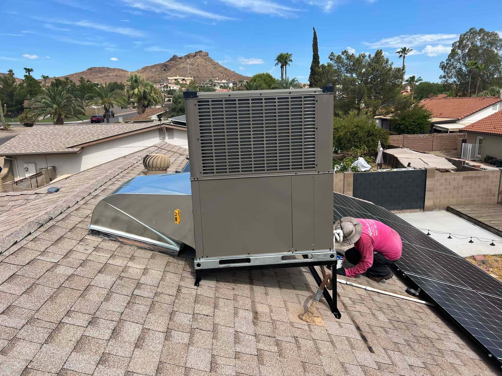 Rooftop package heat pump installed on stands with new duct transition, as a technician secures piping and connections.