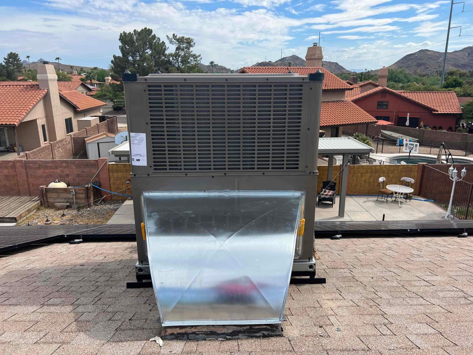 Rooftop package heat pump newly set on curb with sealed sheet-metal transition ductwork over shingle roof.