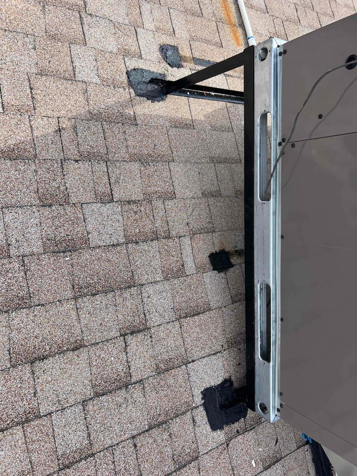 Rooftop package unit secured on a metal stand with roof penetrations sealed with roofing mastic around mounting legs.