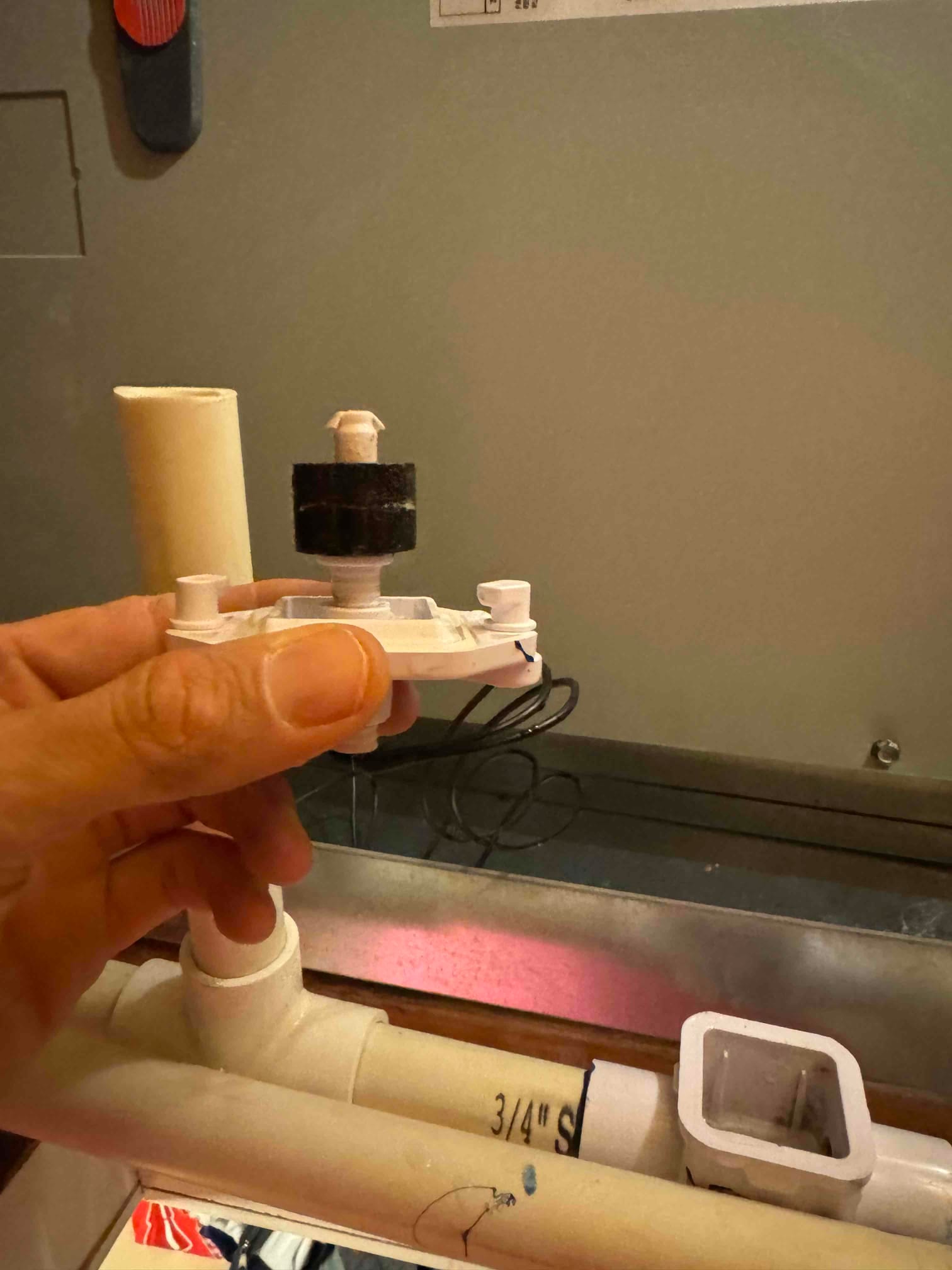 Technician holds a float switch removed from a condensate drain line near the air handler during drain repair.