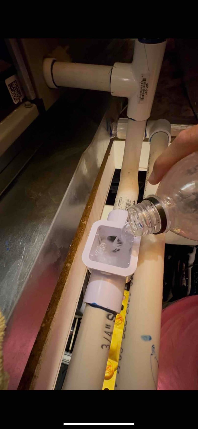 Technician pours cleaning solution into a condensate drain line access fitting on PVC piping inside the air handler.