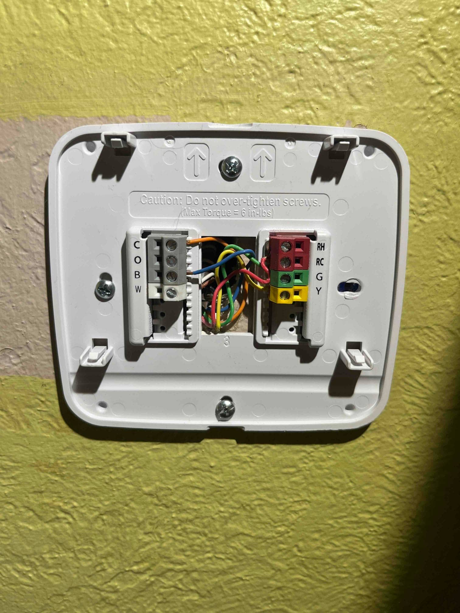 Thermostat wall plate with exposed low-voltage wiring connected to labeled terminals R, RC, G, Y, C, O, B, and W.