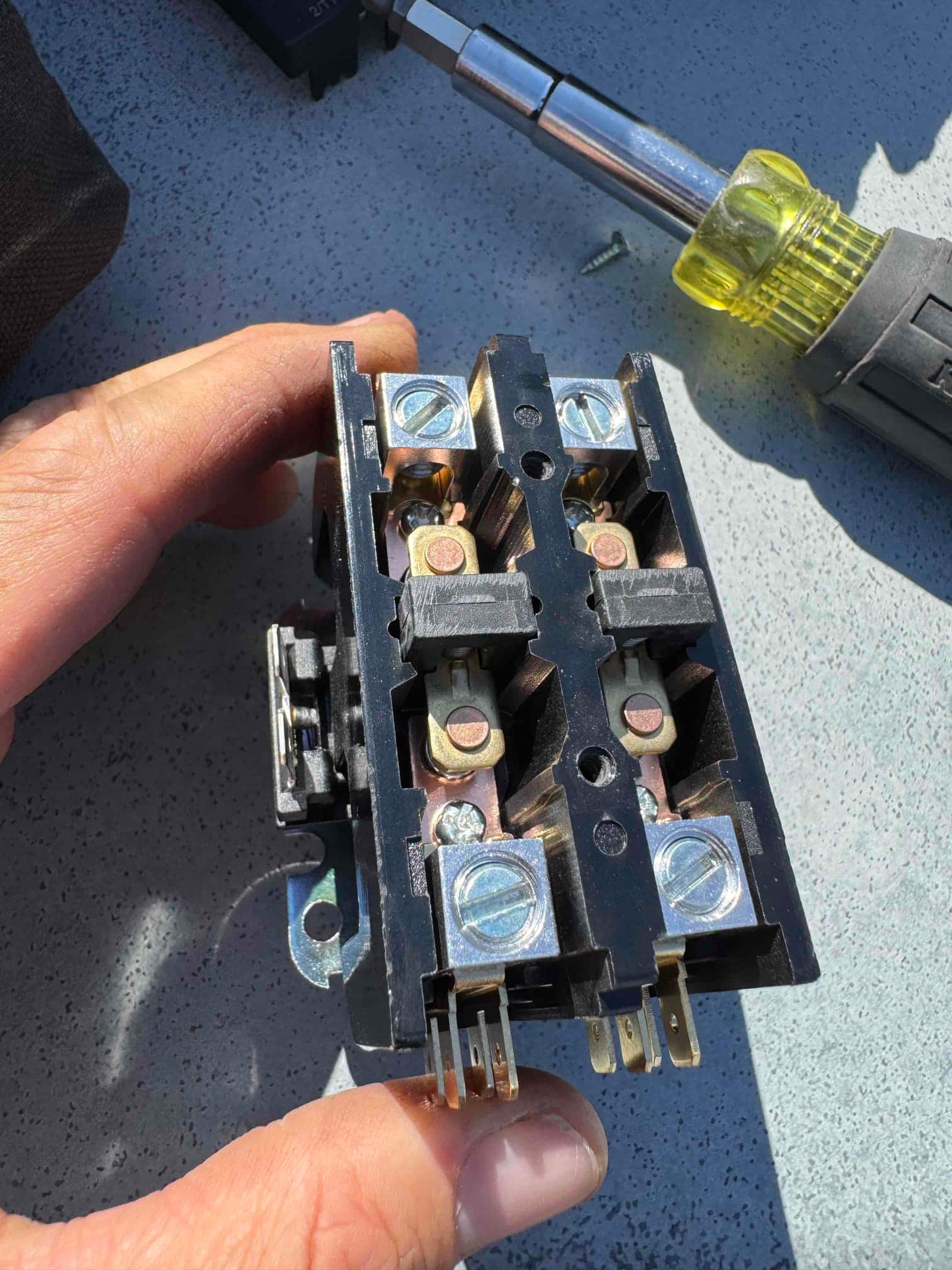 Used 2-pole contactor removed from an air conditioner, showing worn contact points and coil terminals held by a technician’s hand.