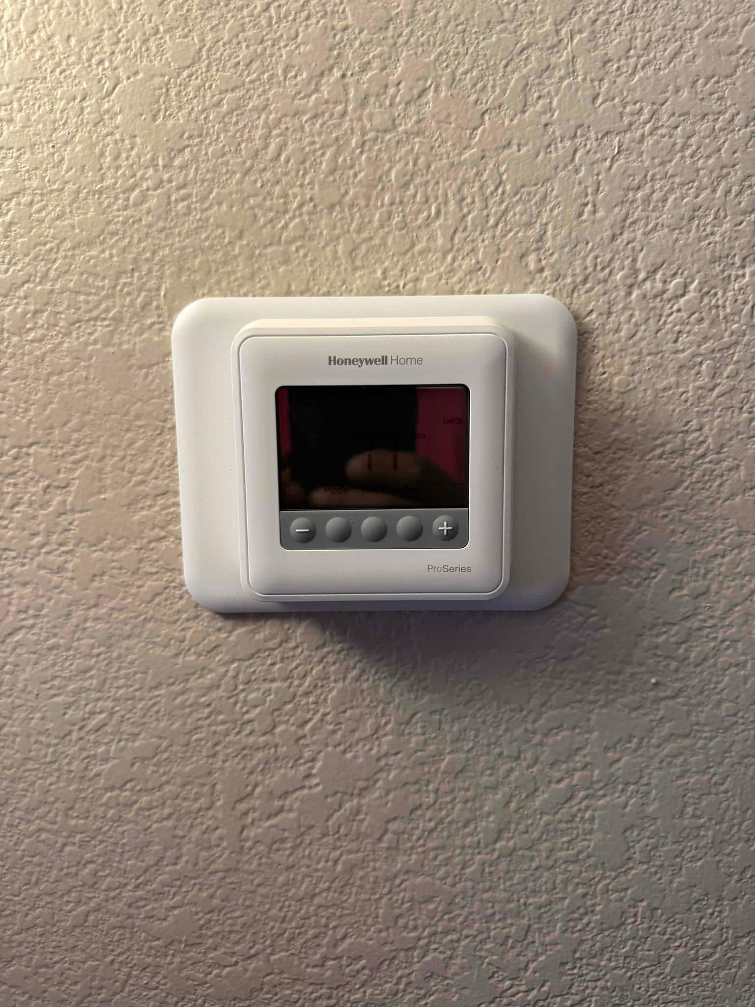 Wall-mounted programmable thermostat installed and powered, showing control buttons and display within a clean trim plate.