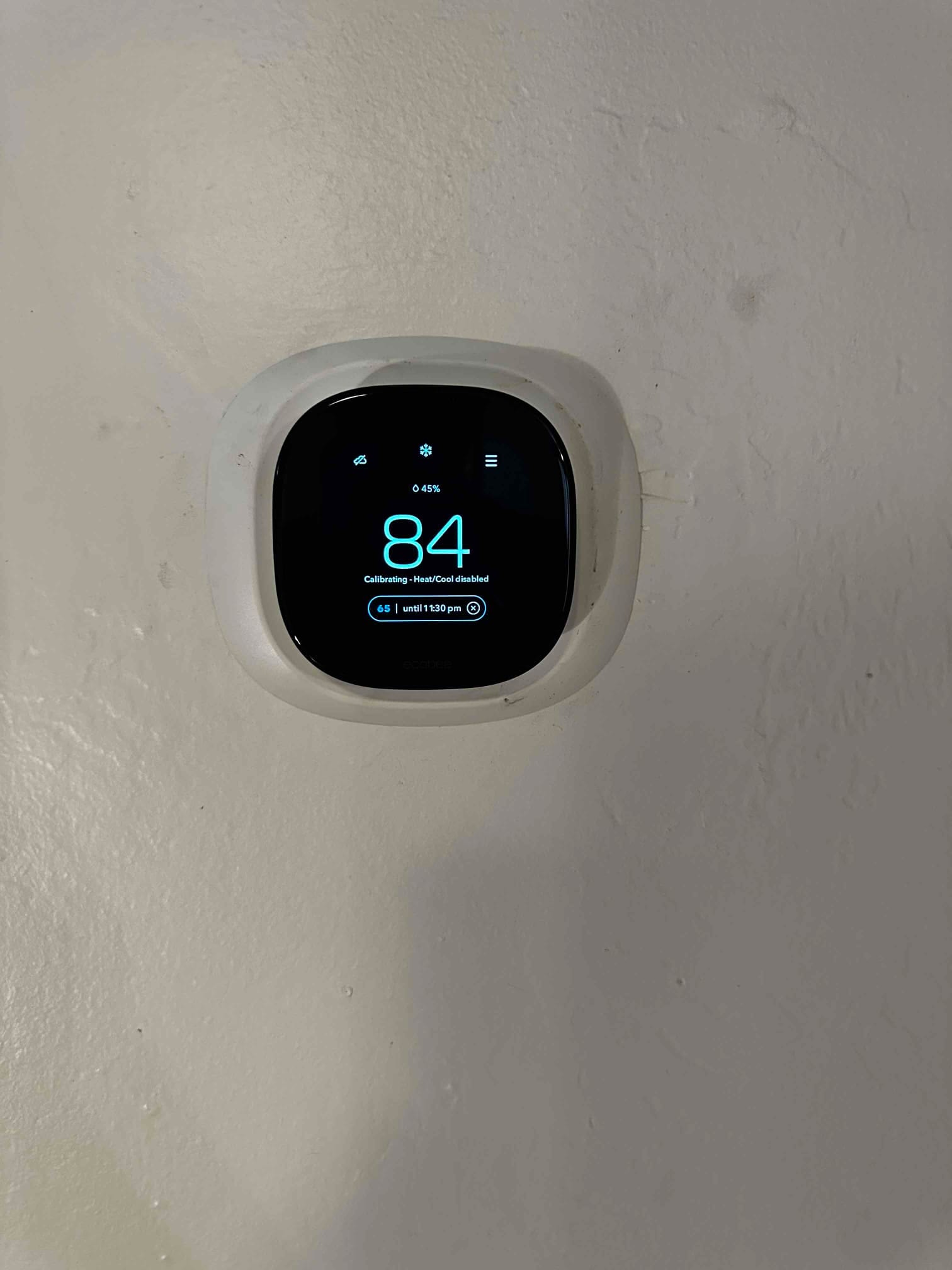 Wall-mounted smart thermostat displays 84 degrees and shows a calibration message during setup after installation.