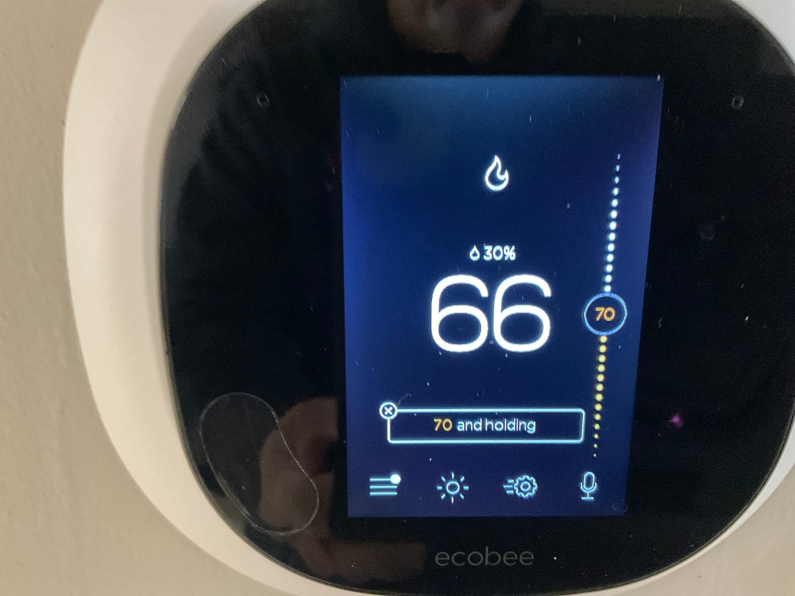 Wall-mounted smart thermostat displays indoor temperature of 66 degrees with a setpoint of 70 and system status icons.