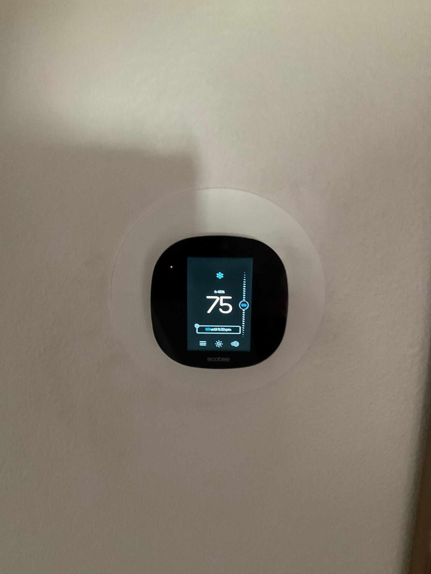 Wall-mounted smart thermostat powered on, showing cooling mode with a setpoint of 75 degrees and interface illuminated.
