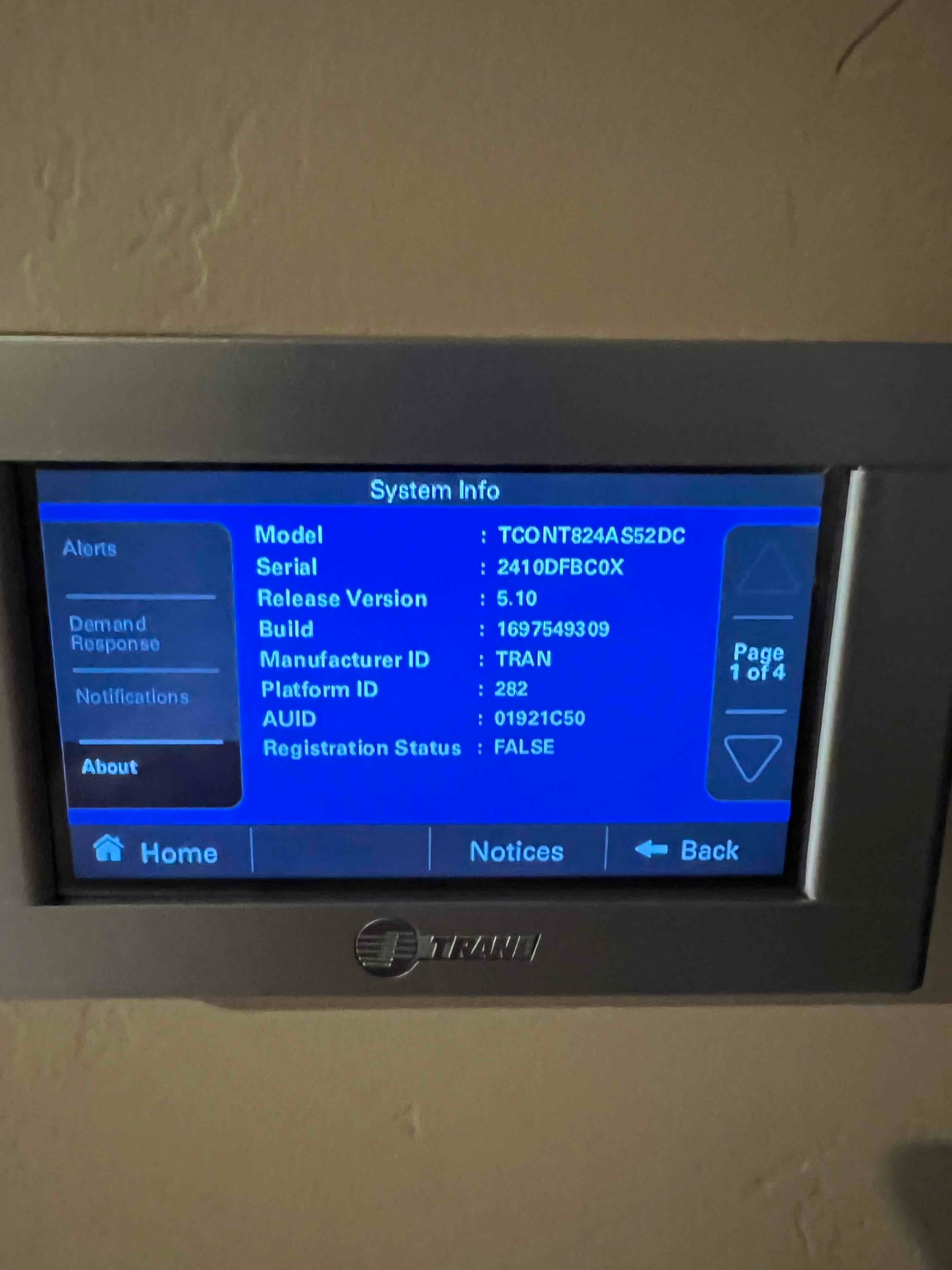 Wall-mounted thermostat displays system information screen after installation, showing menu options and device details on the interface.