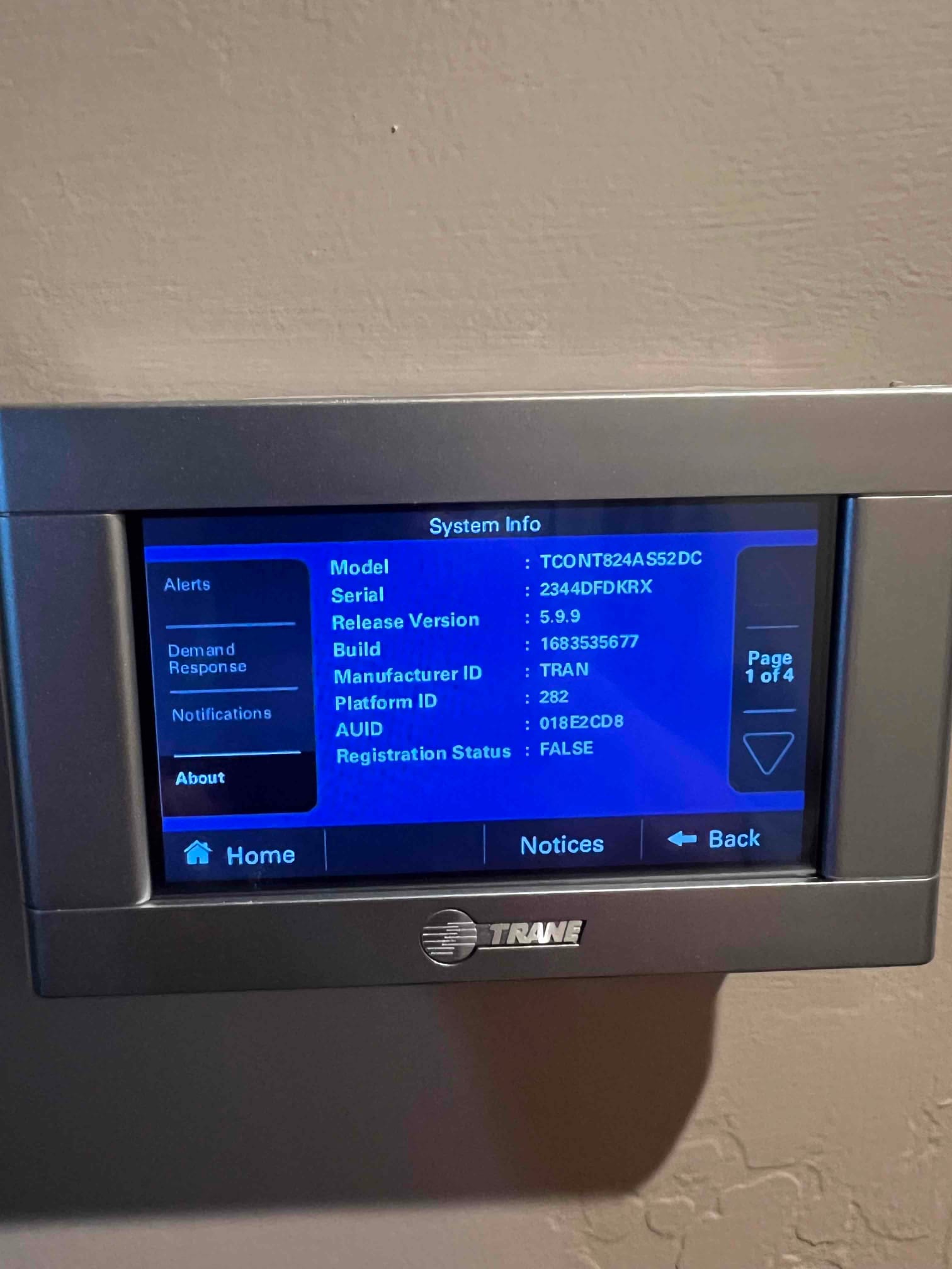 Wall-mounted thermostat displays system information screen with model, serial, and software details after installation setup.