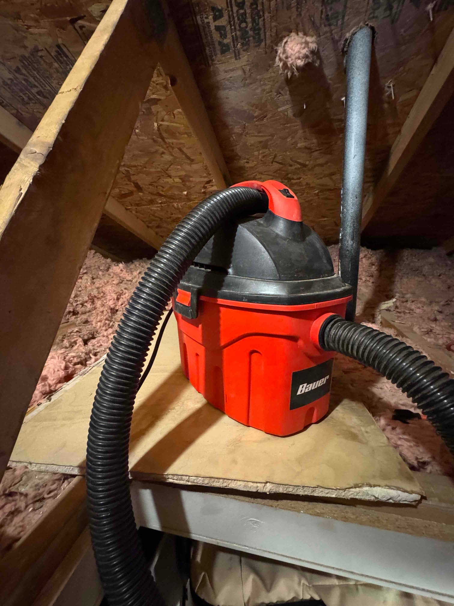 Wet/dry vacuum set up in an attic near insulation, used to clear a clogged condensate drain line.