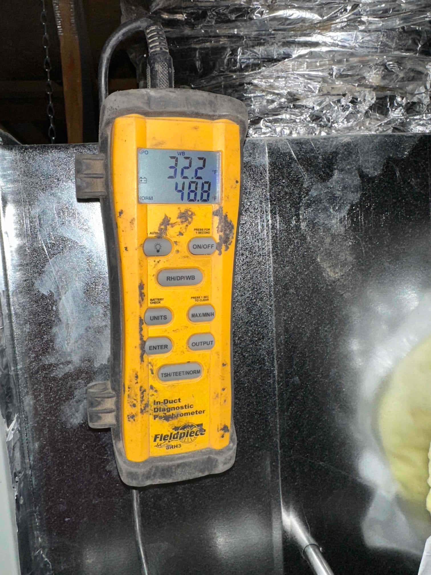 Digital in-duct thermometer displays 32.2 and 48.8 readings while measuring air conditions at the supply plenum.