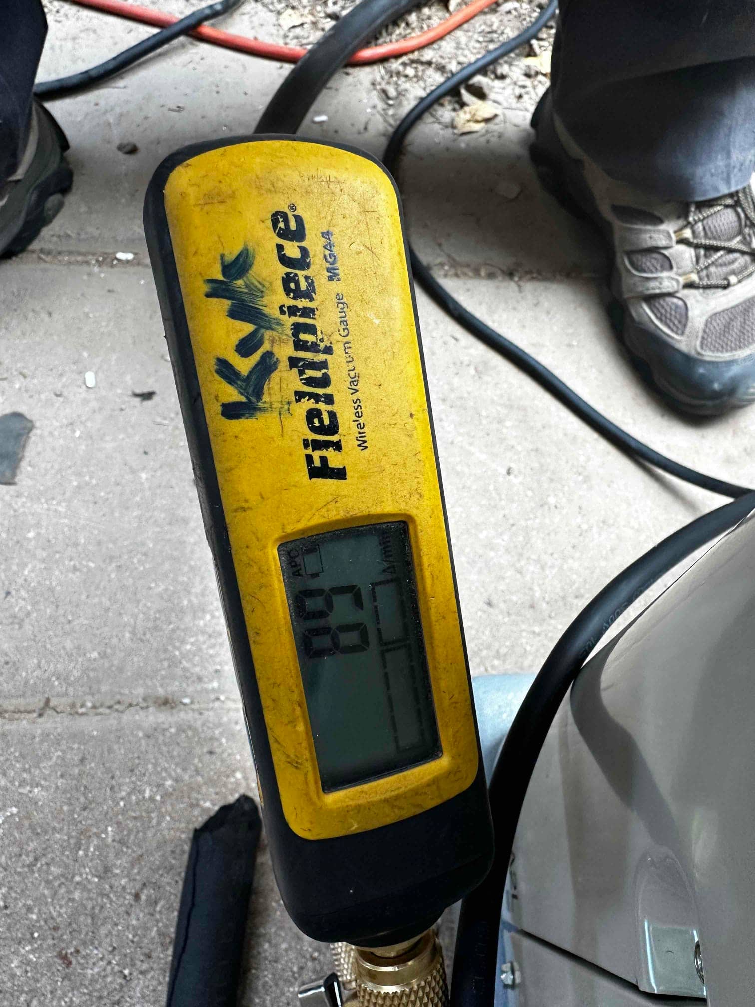 Digital micron gauge attached to the system reads 87 microns, confirming a deep vacuum during the evacuation phase before charging.