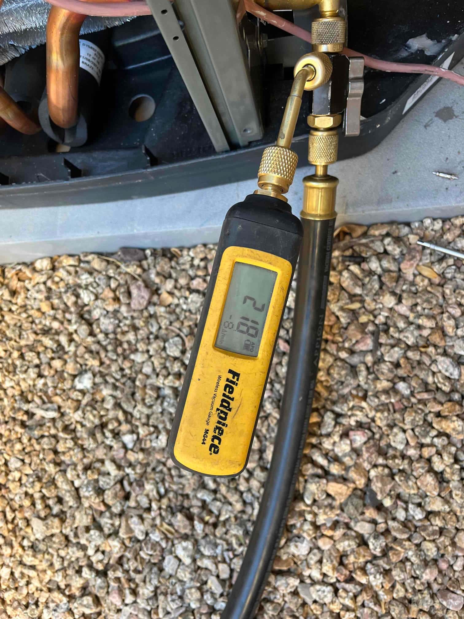 Digital micron gauge connected at the condenser reads 218 microns, confirming a deep vacuum prior to refrigerant charging.