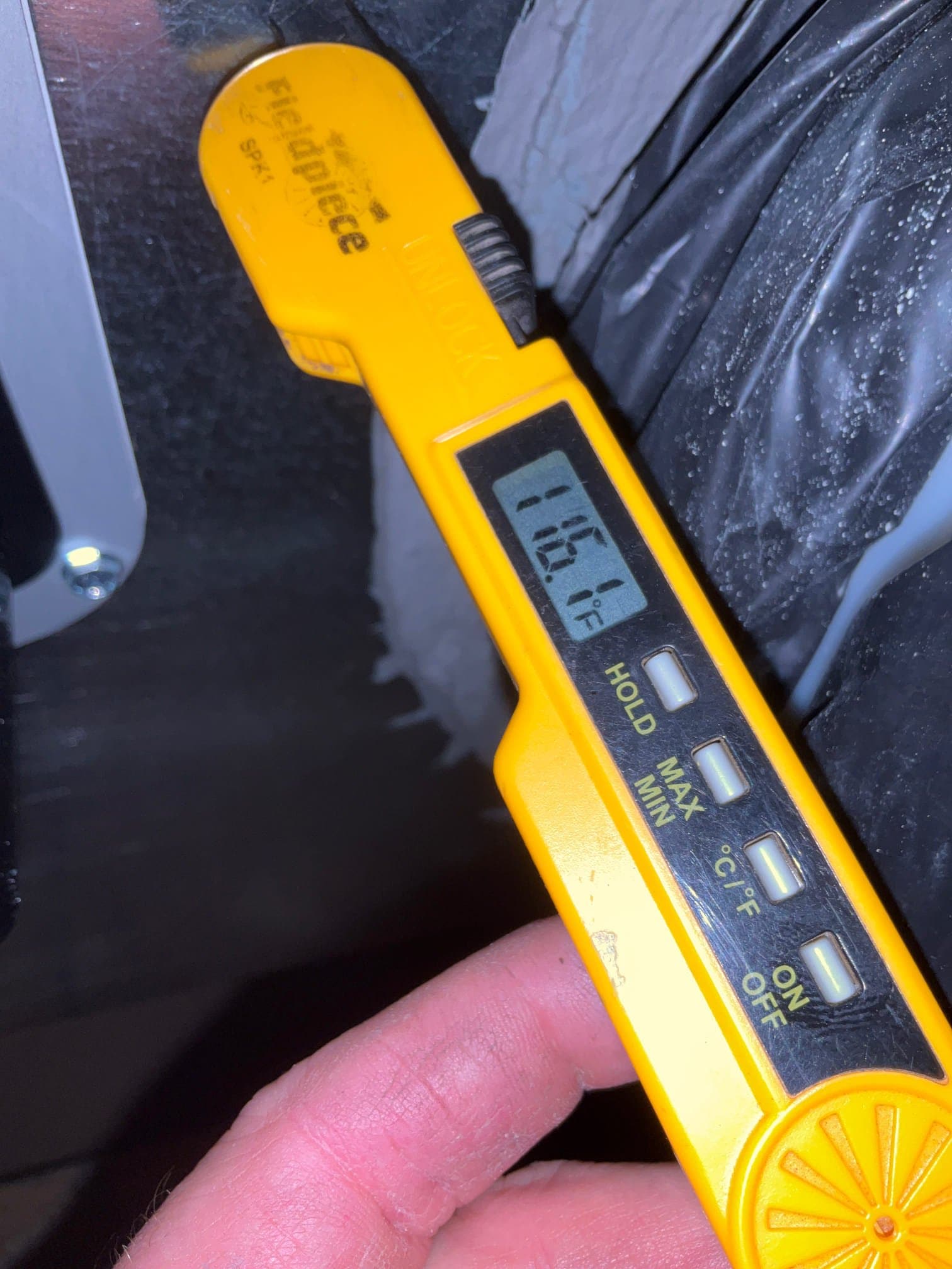 Digital thermometer measures air temperature at the duct connection, displaying 116.1 degrees Fahrenheit during system commissioning.