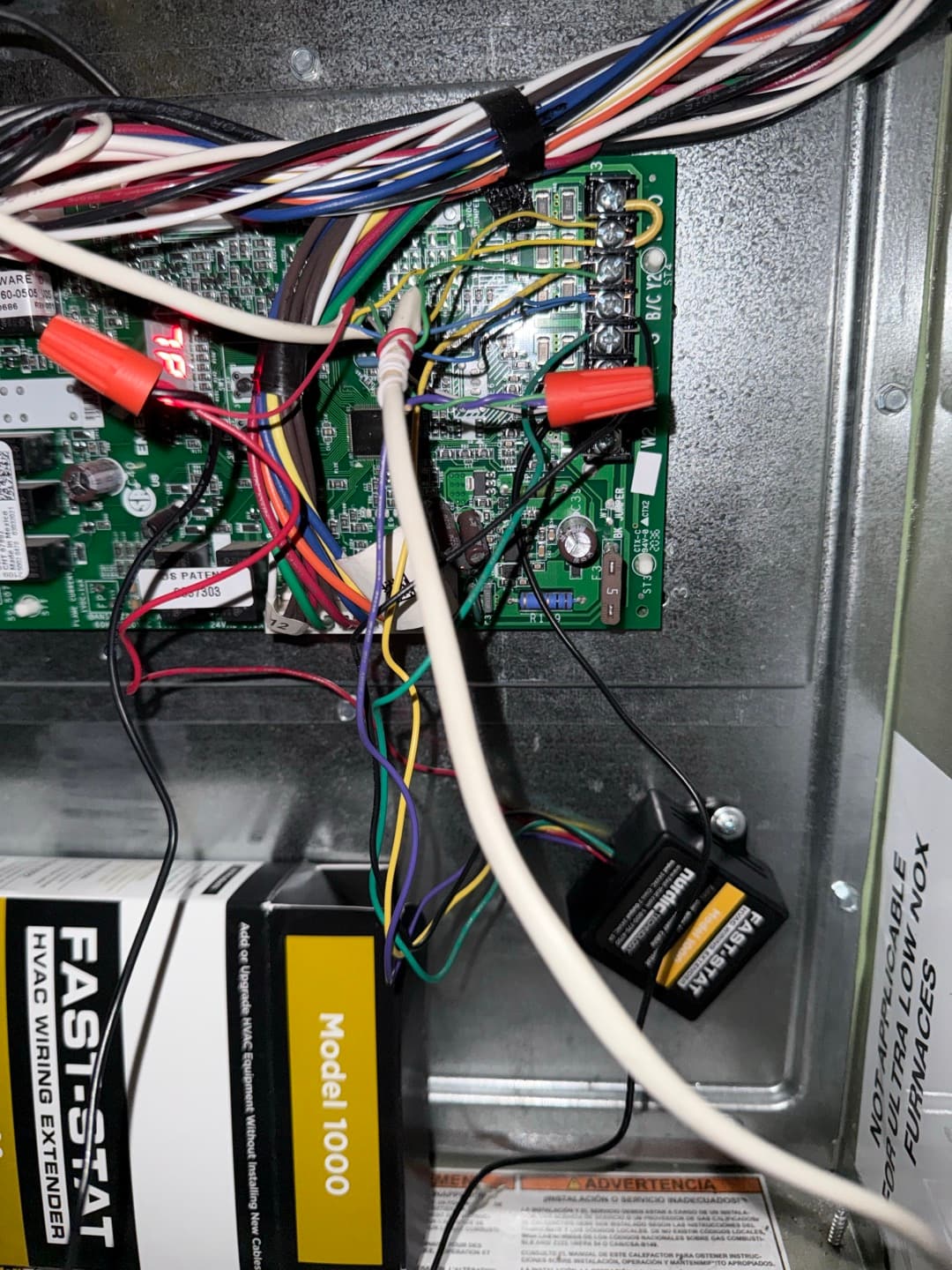 Furnace control board wiring with add-a-wire module installed, showing multiple wire nuts and routed thermostat conductors.