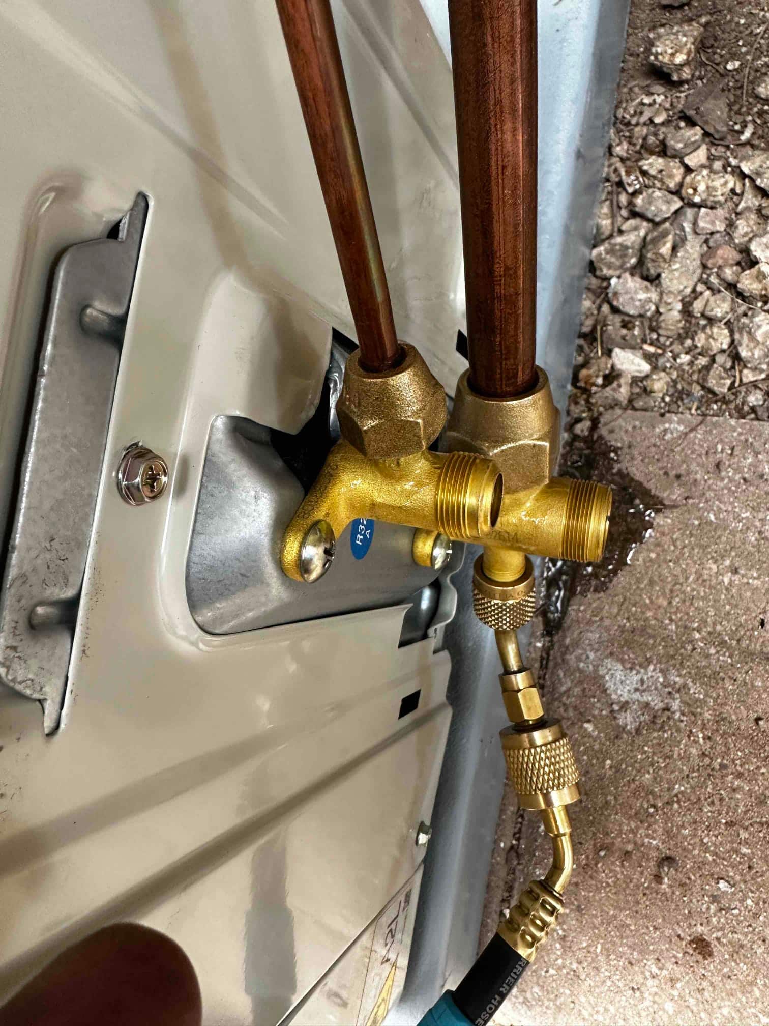 Mini-split outdoor service valves with copper line set connected and a hose attached to the service port during installation.