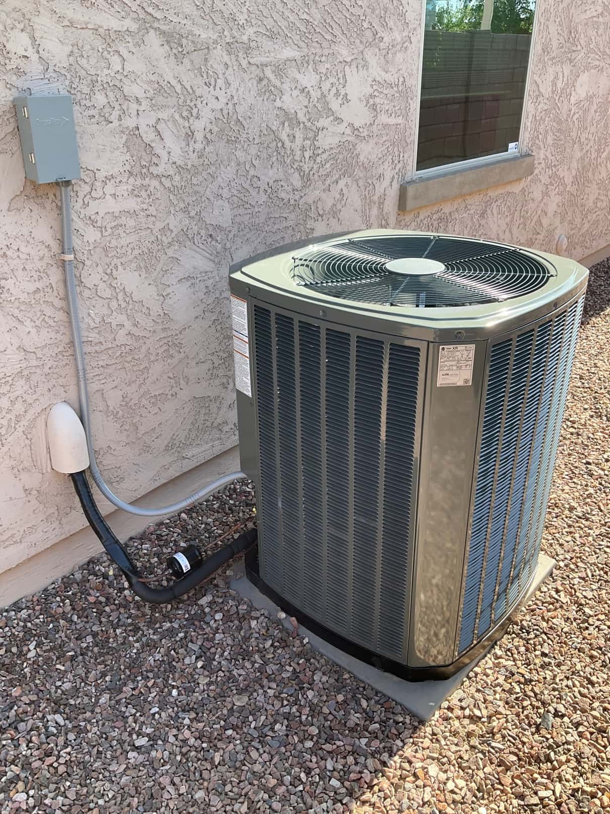 New outdoor condenser set on a level pad with sealed line set cover and installed electrical disconnect on the wall.