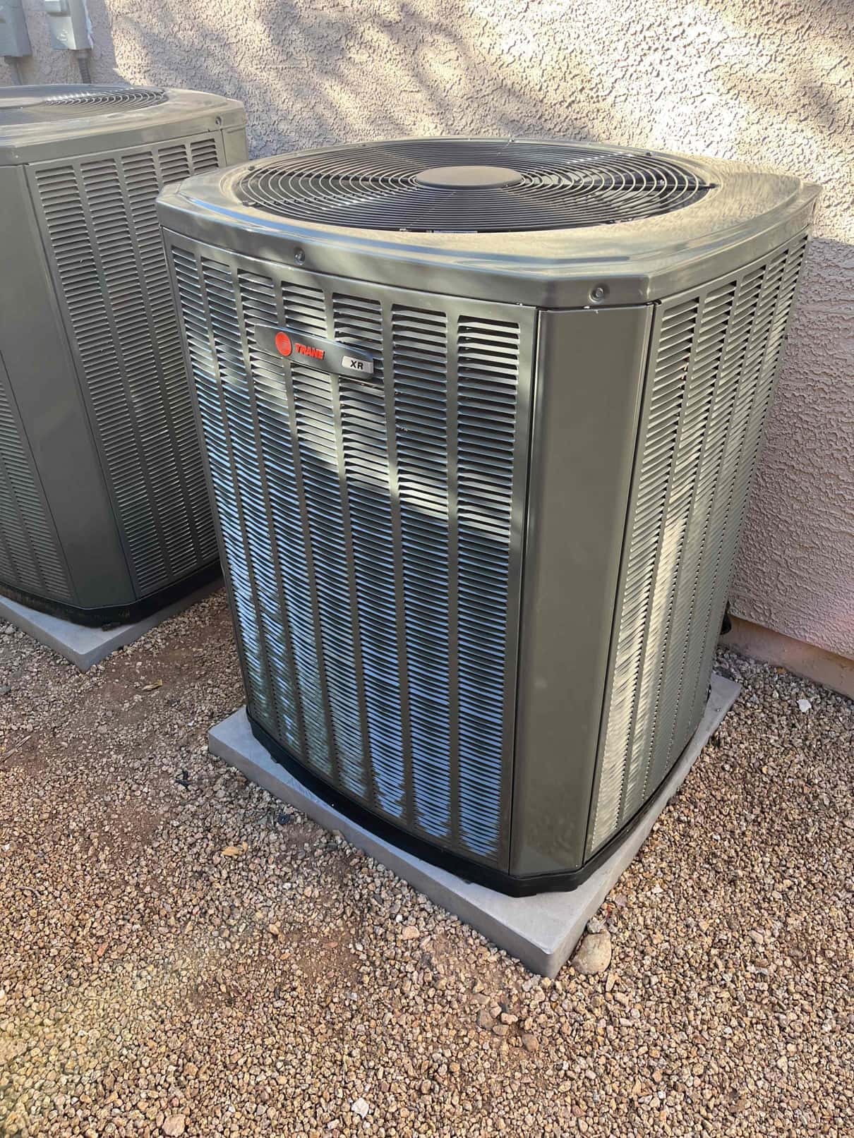 New outdoor condensers set on level pads beside the home, with protective grilles and clean surrounding gravel base.