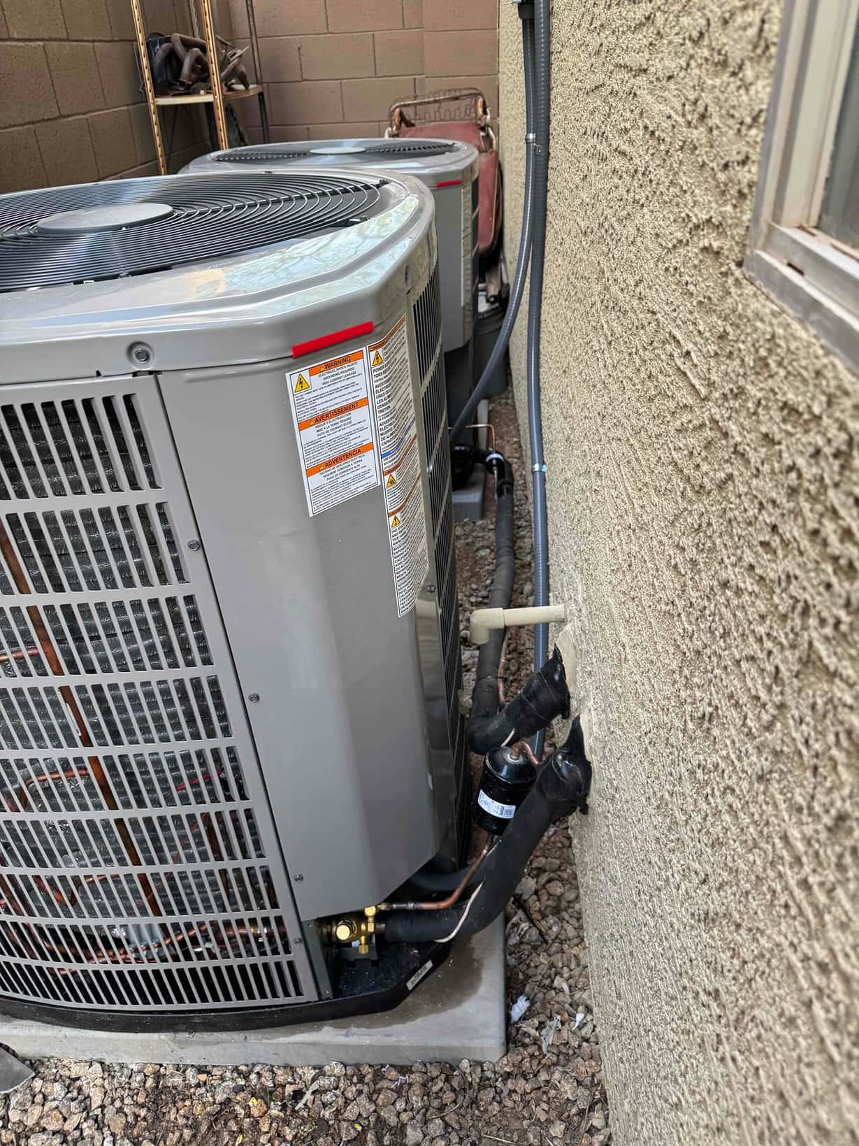 Two newly installed outdoor condensers on level pads with insulated line sets, filter-driers, and sealed wall penetrations along the exterior wall.