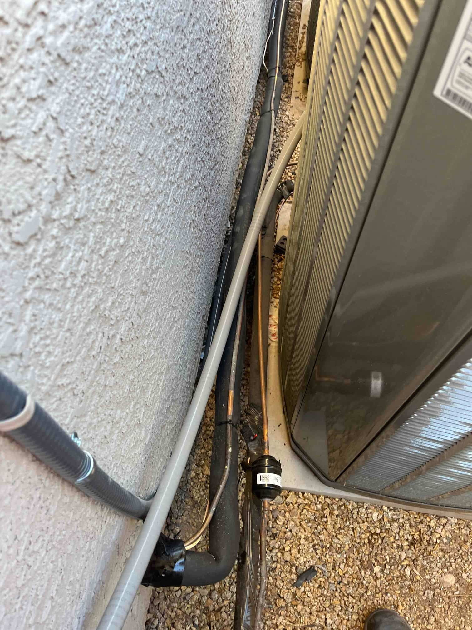 Outdoor condenser with insulated refrigerant line set, condensate drain, and electrical conduit neatly routed along the wall and pad.