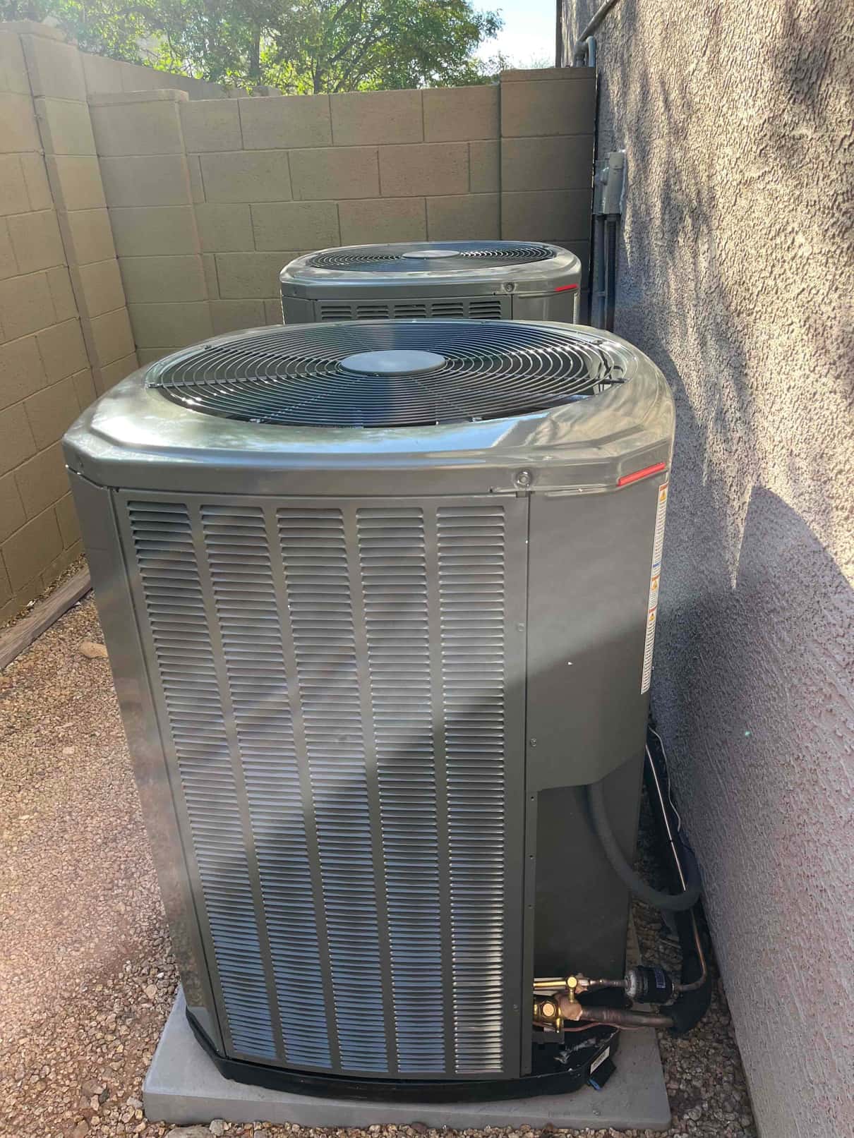 Two outdoor condenser units set on level pads with insulated refrigerant lines and electrical disconnects mounted on the wall.