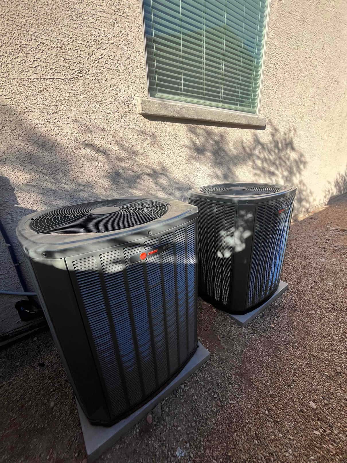 Two outdoor condensers set on level pads beside the home, with insulated refrigerant lines routed to the wall penetration.