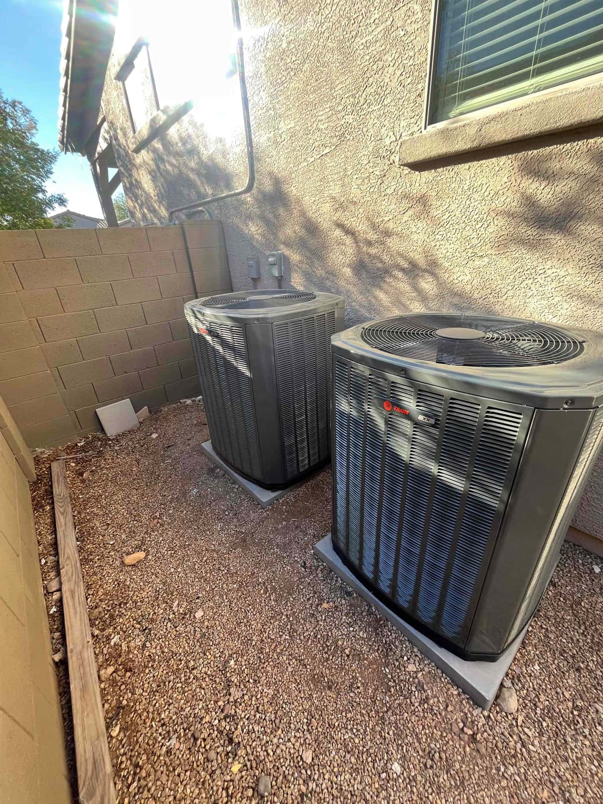 Two outdoor condensers set on level pads beside the home with line sets and disconnects mounted on the wall.