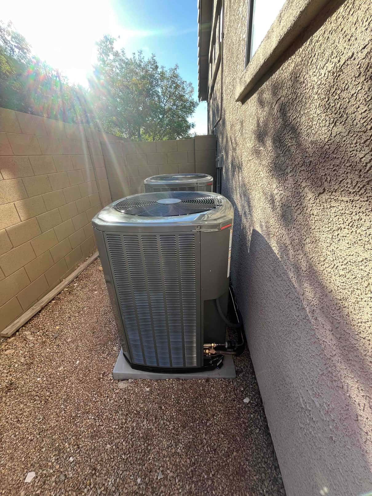 Two outdoor condensers set on level pads beside the house with connected refrigerant lines and proper clearances.