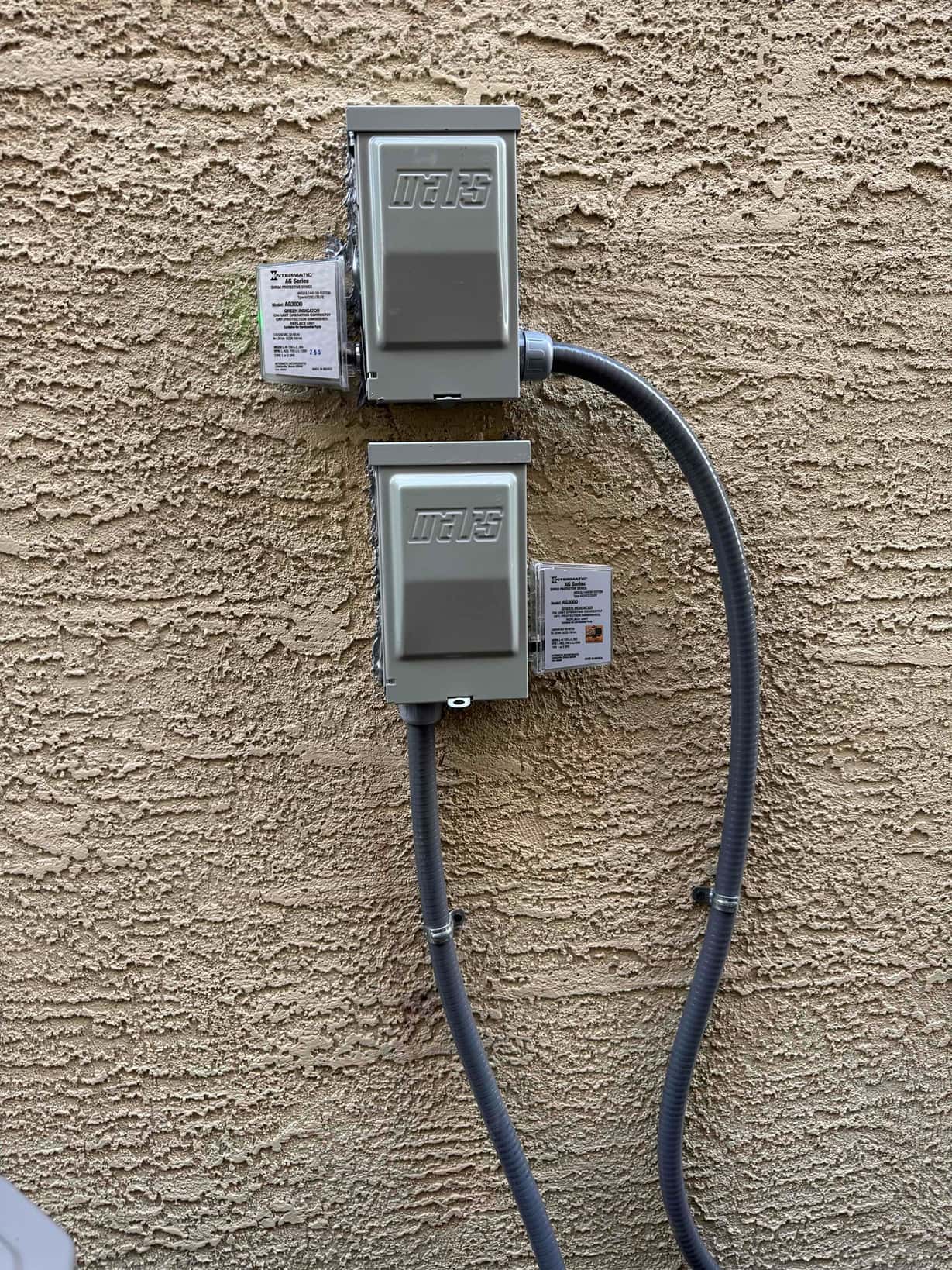 Two outdoor HVAC disconnect boxes mounted on stucco with flexible conduit neatly routed and secured to the exterior wall.