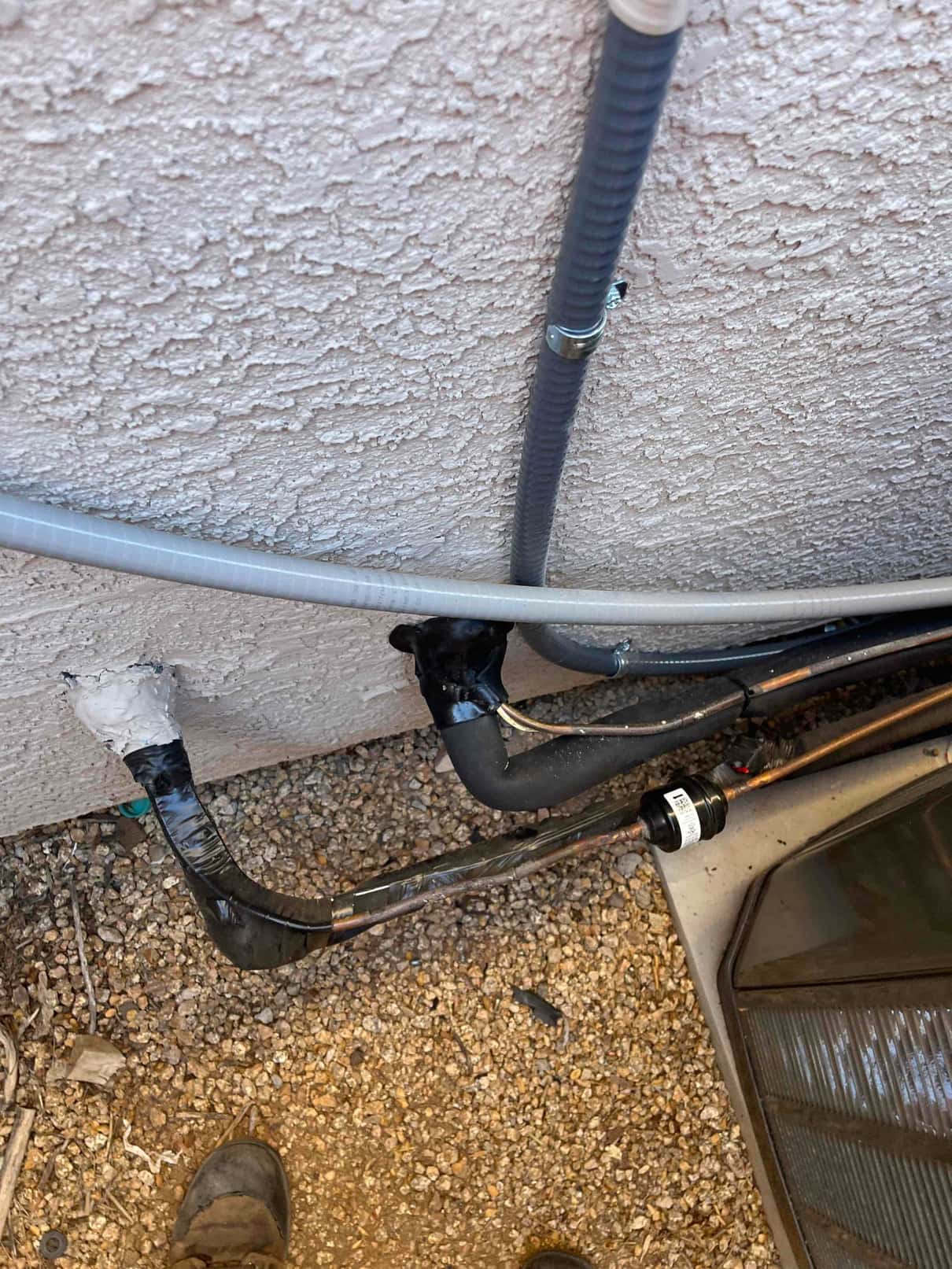 Refrigerant line set and condensate drain routed through sealed wall penetration beside the outdoor condenser with protective insulation and straps.