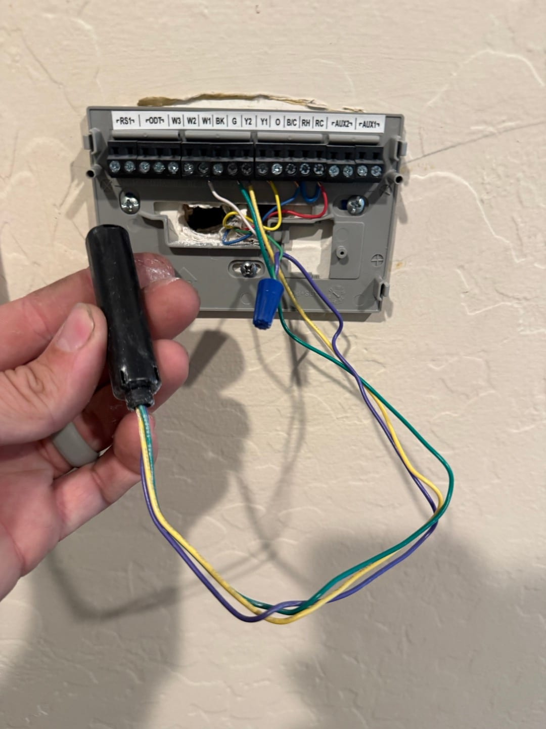 Thermostat sub-base with exposed low-voltage wiring and an add-a-wire module held next to the terminal strip.