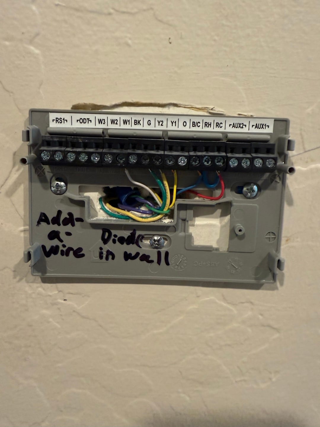 Thermostat sub-base with exposed low-voltage wiring and labeled terminals, showing add-a-wire diode connection noted on the wall.