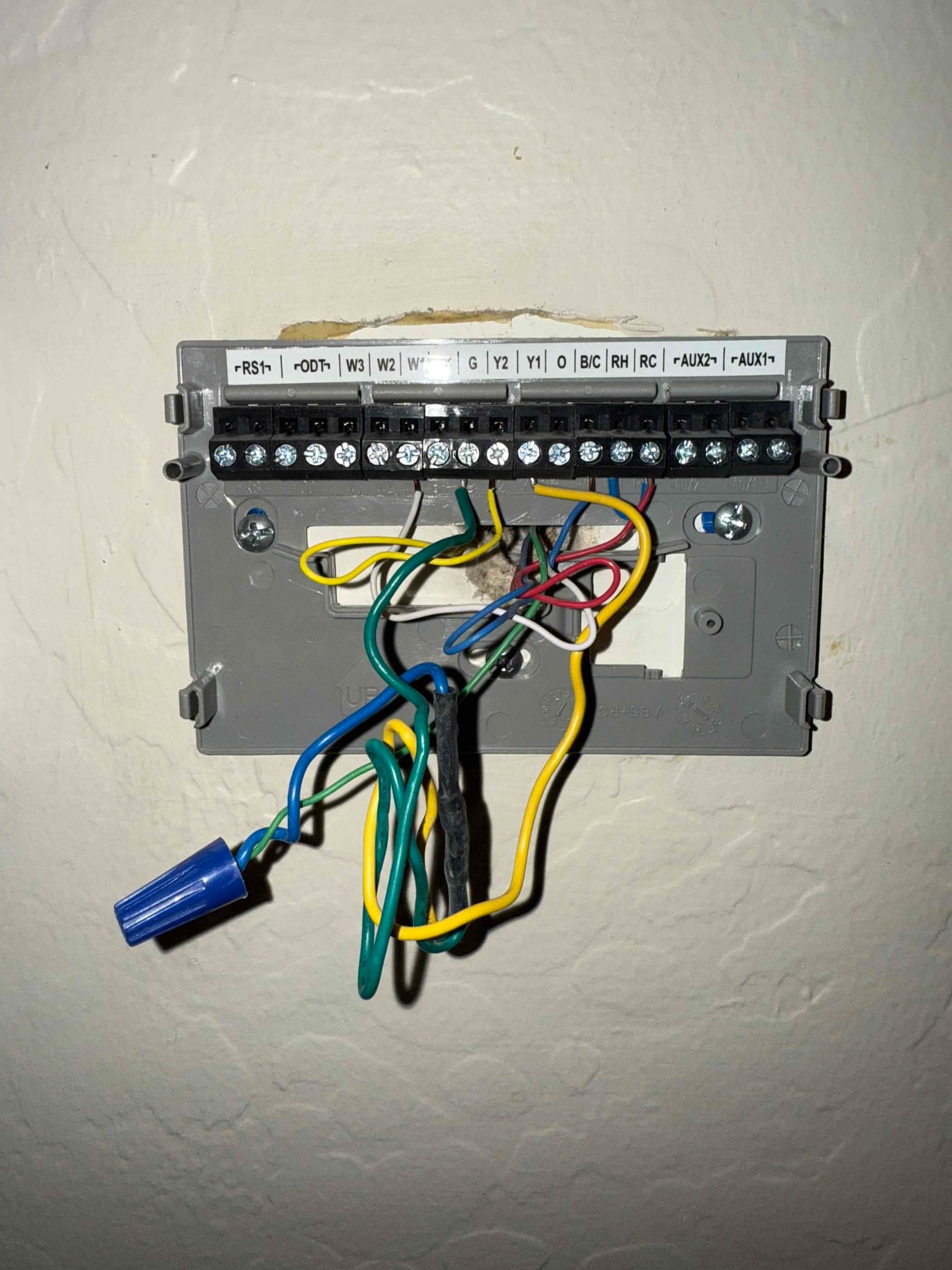 Thermostat sub-base with exposed low-voltage wiring and labeled terminals, showing wire nut splice and add-a-wire module connections.