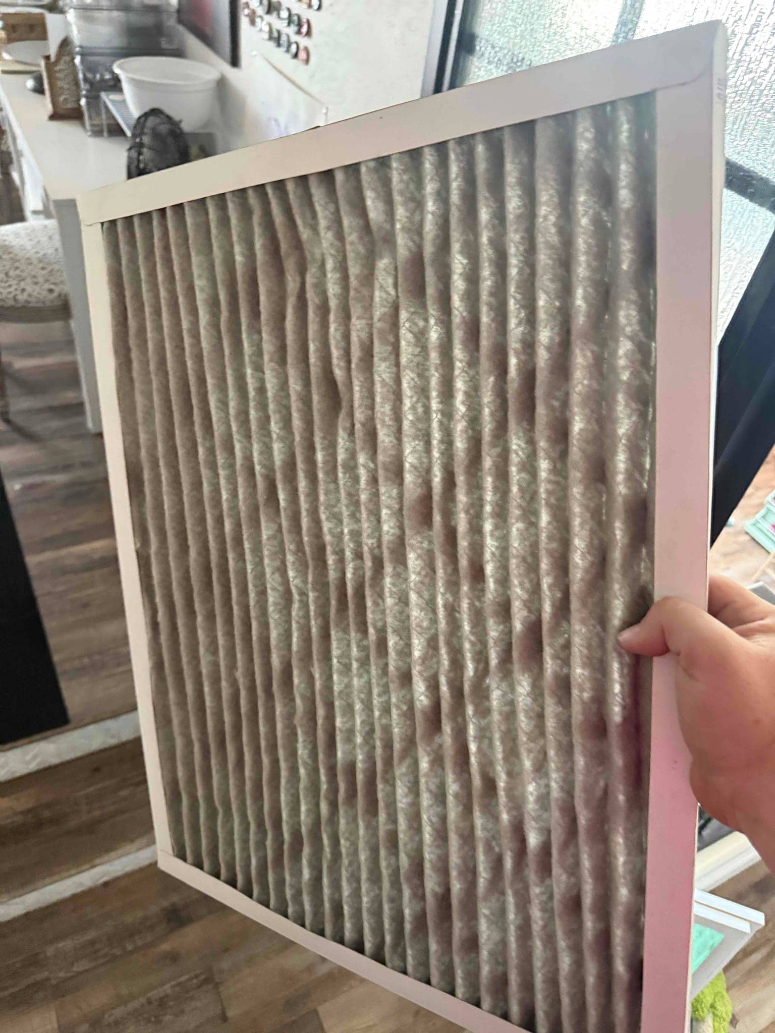Used pleated air filter held by hand, showing accumulated dust across the media and intact cardboard frame.