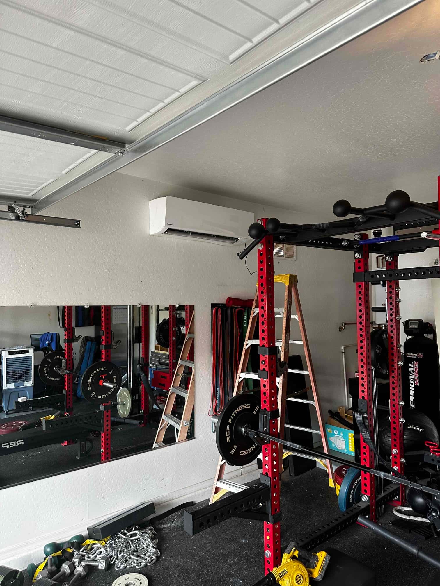 Wall-mounted mini-split indoor unit installed in a garage gym, with ladders and equipment visible after installation work.